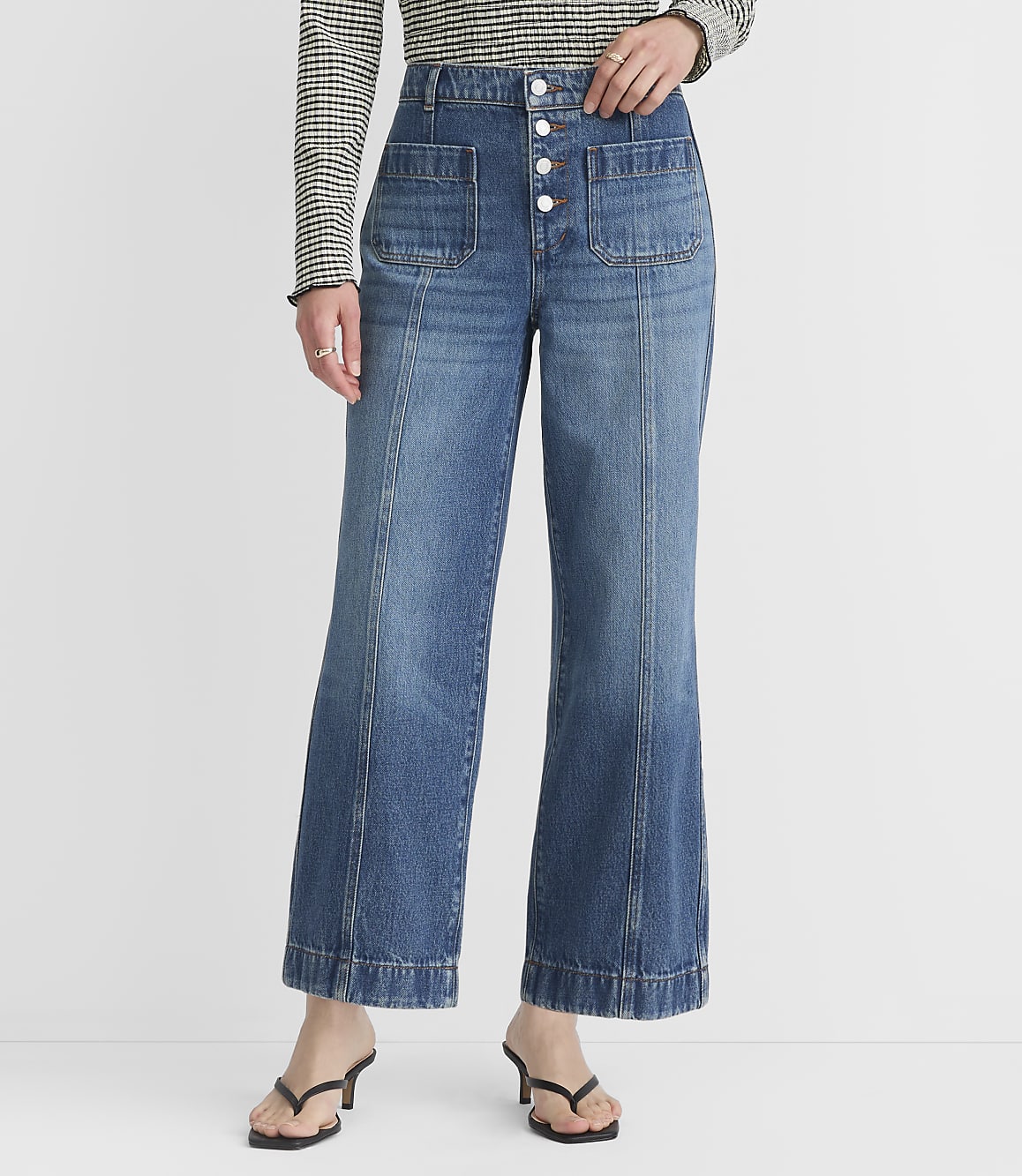 A person wearing high-waisted, wide-leg blue jeans with front pockets and a white button-up fly stands against a plain white background.