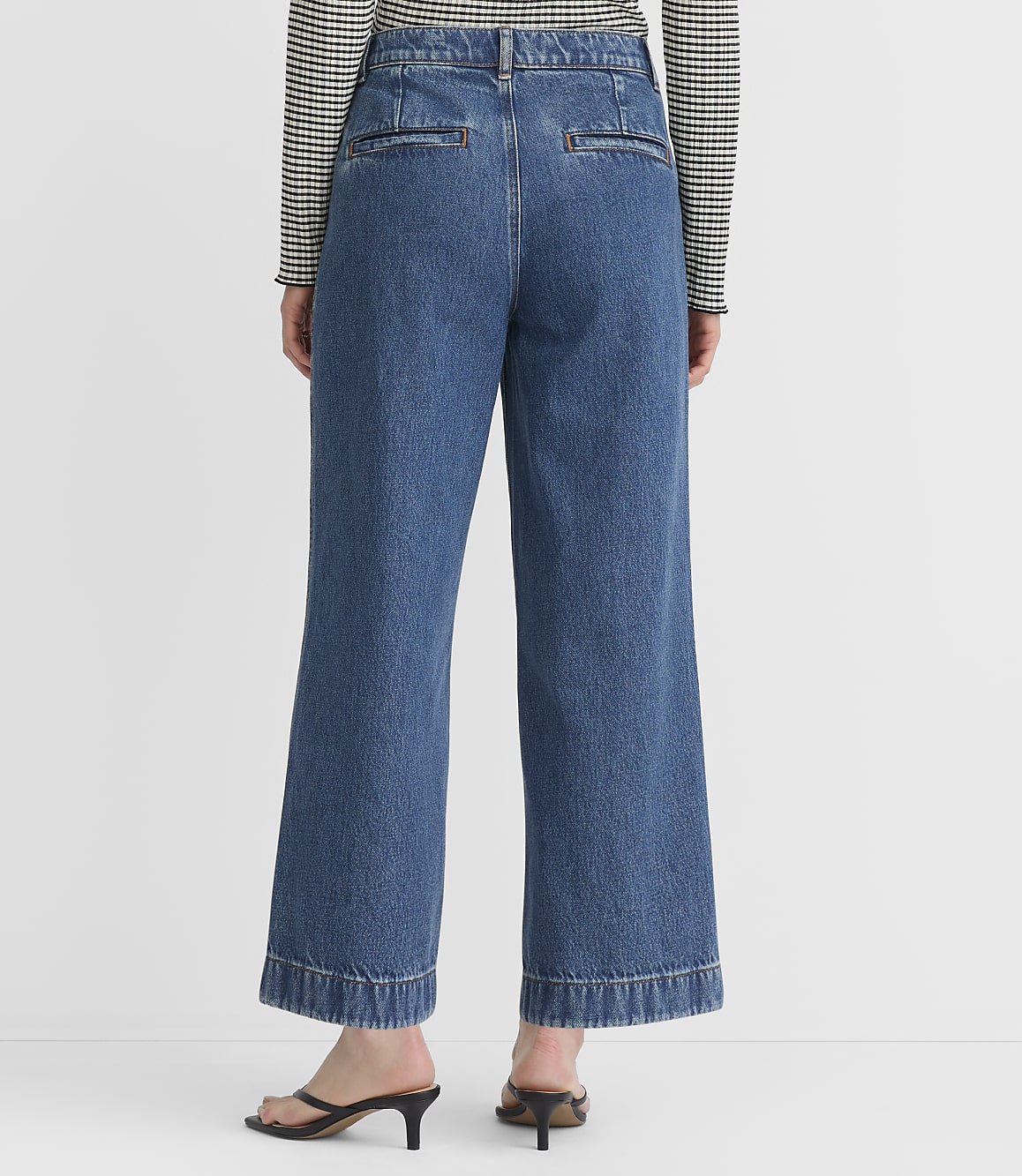 A person wearing wide-leg denim jeans and a striped shirt stands against a plain white background.