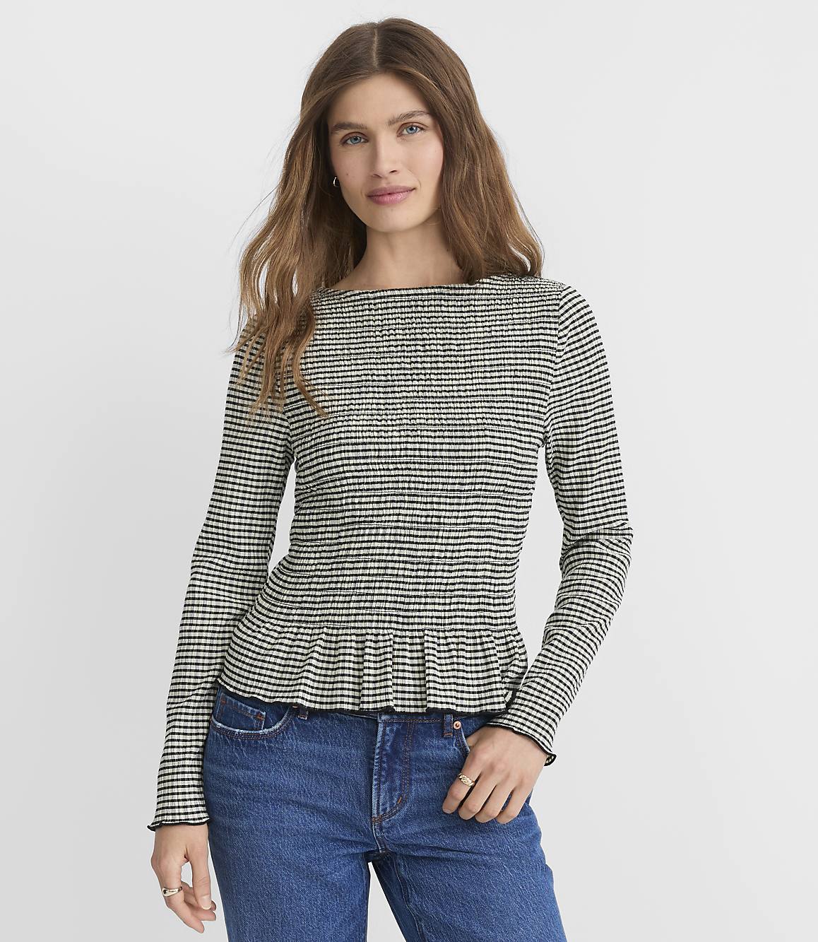 A woman in a black and white checkered peplum top and blue jeans stands against a plain white background.