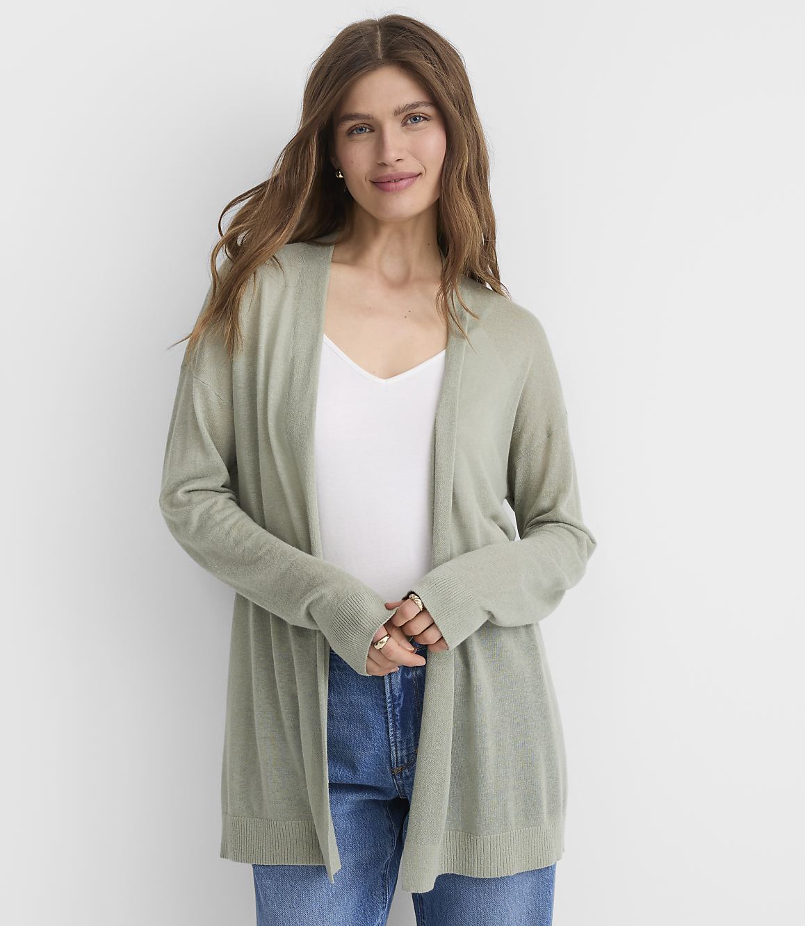 A woman in a light green cardigan and blue jeans stands against a plain white background.
