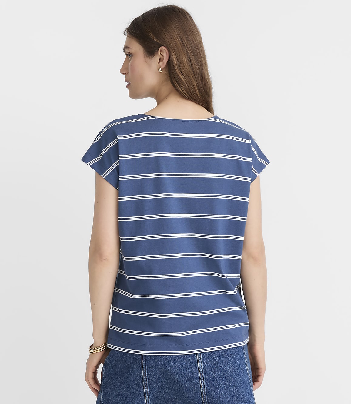 A woman in a blue and white striped shirt and denim skirt stands against a plain white background.