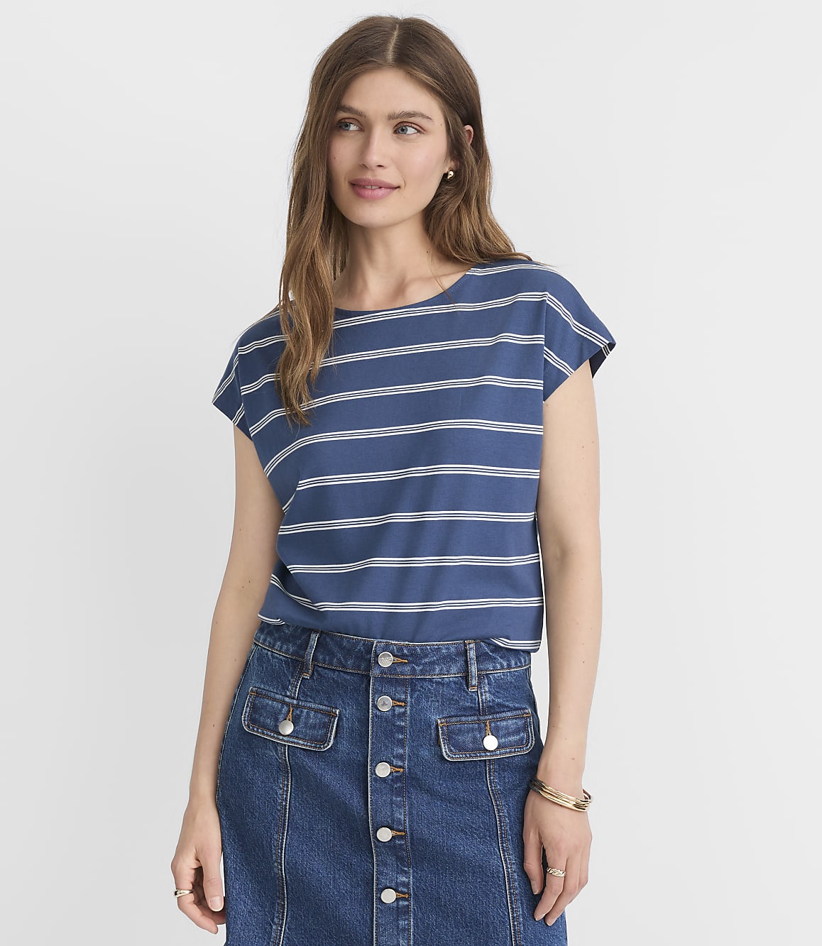 A woman in a blue and white striped t-shirt and denim skirt stands against a plain white background.