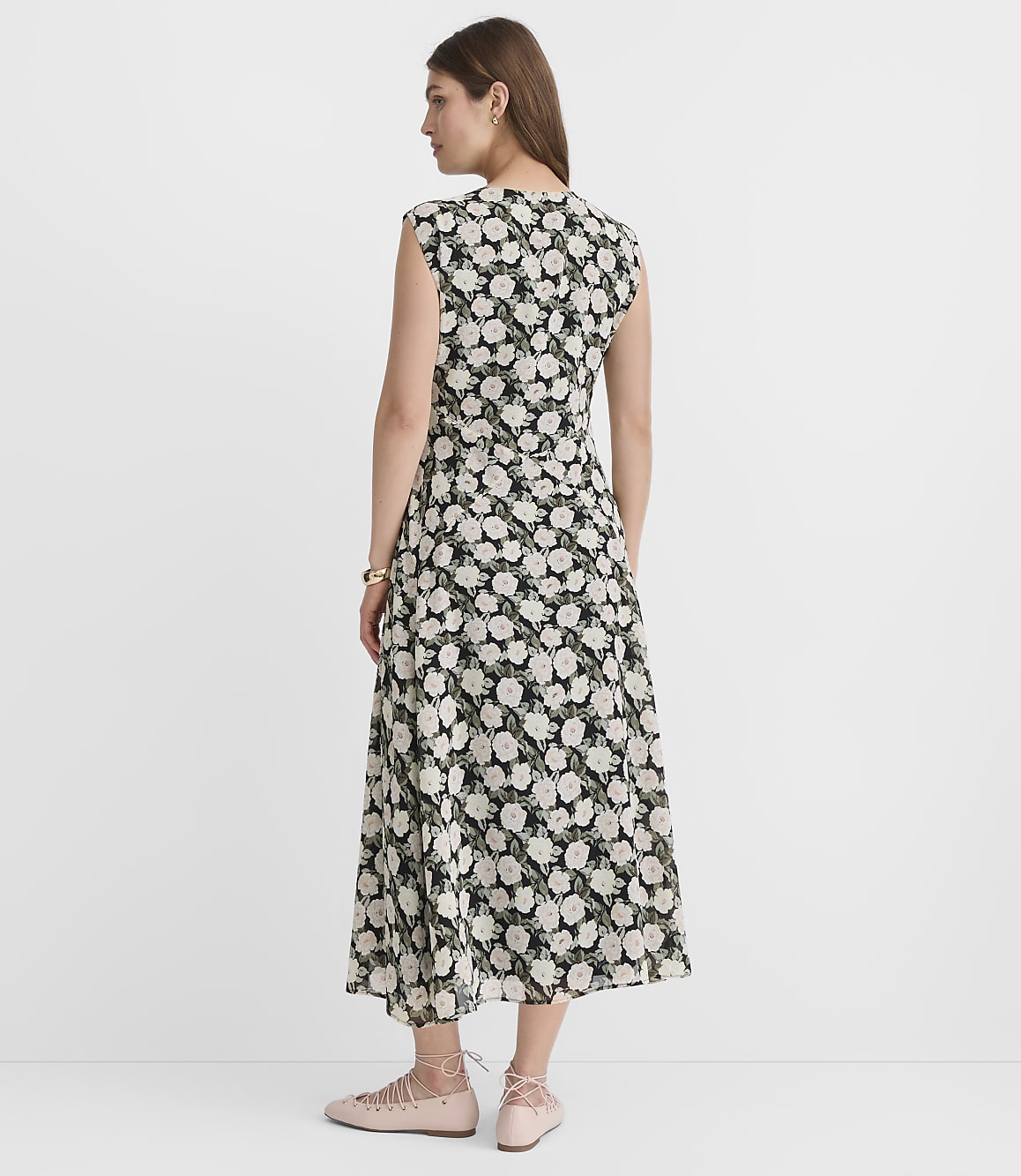 A woman in a floral dress stands against a plain white background.