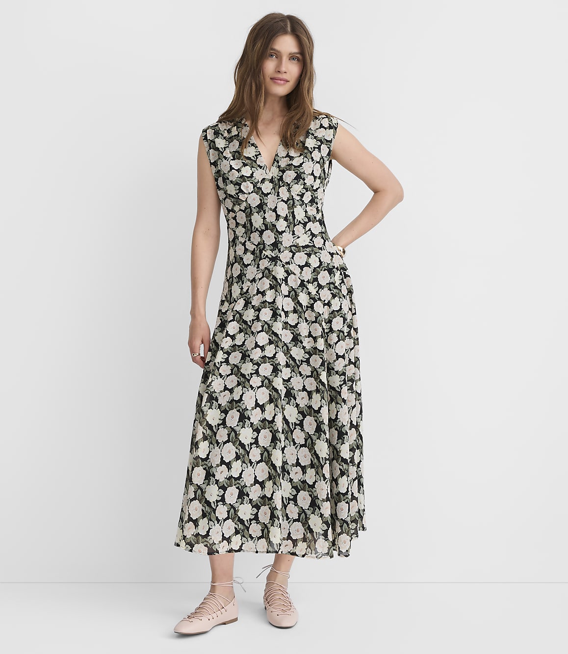 A woman in a floral dress stands against a plain white background.