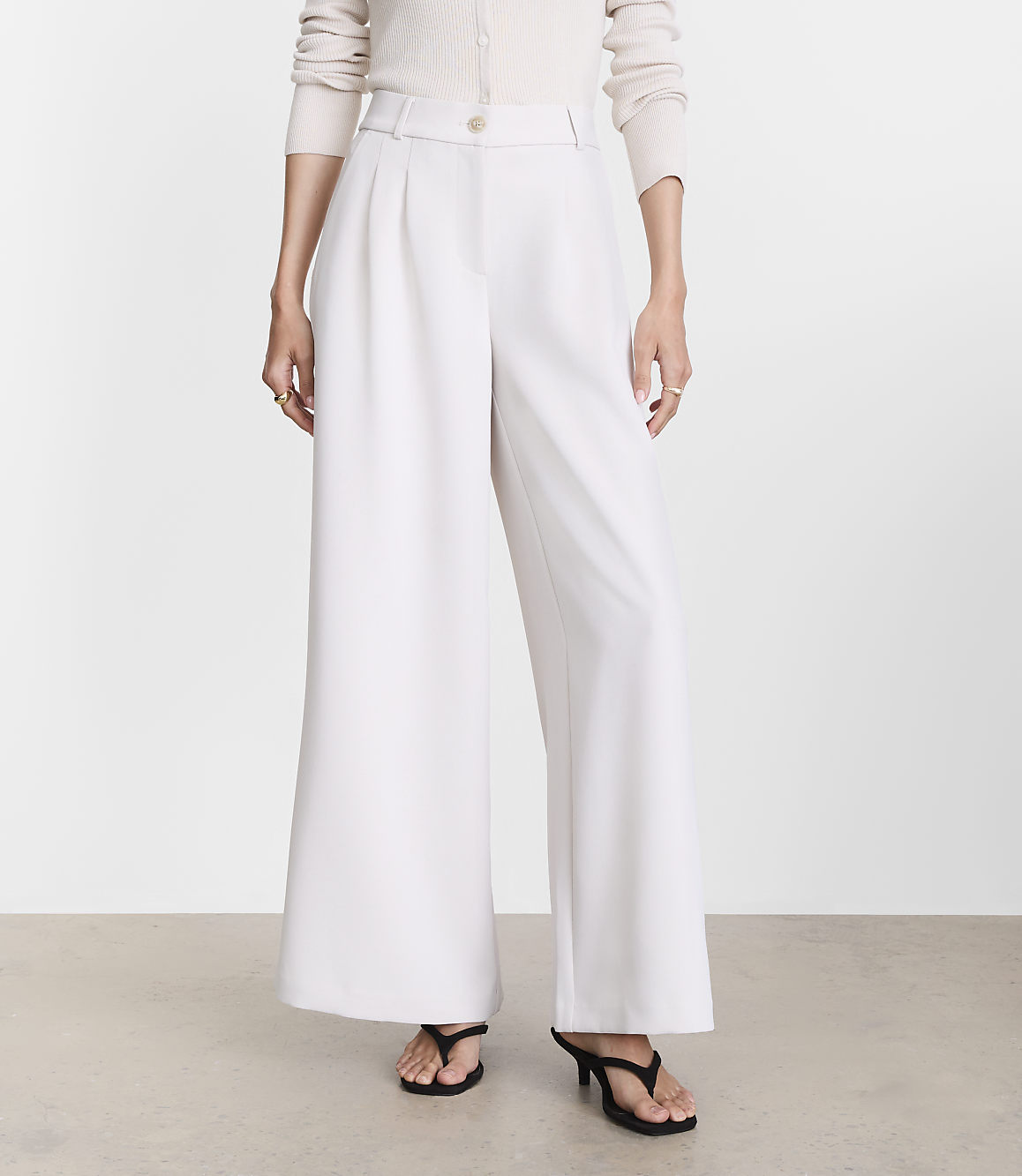 A person stands in wide-leg white pants and black heels against a plain white background.
