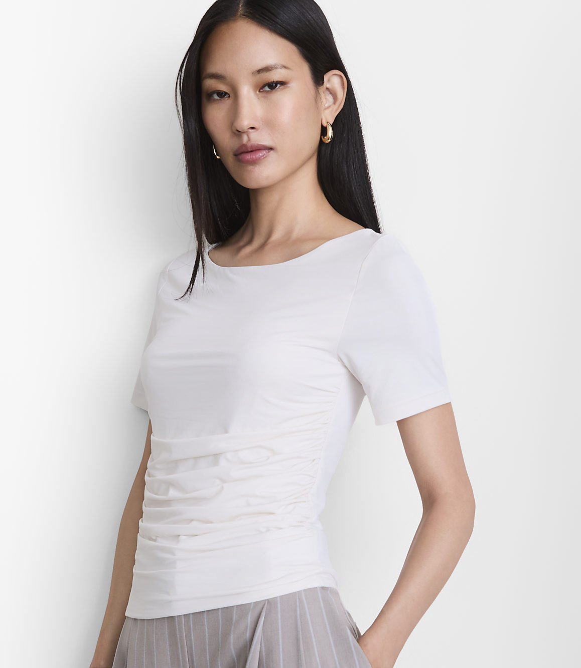 A woman in a white ruched t-shirt and striped pants stands against a plain white background.