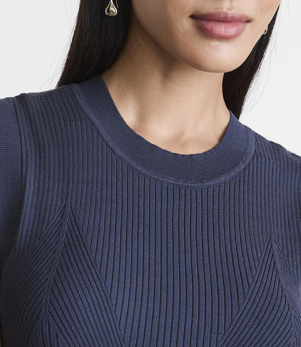 A close-up of a woman's neck and shoulders wearing a navy blue ribbed sweater, with a blurred background.