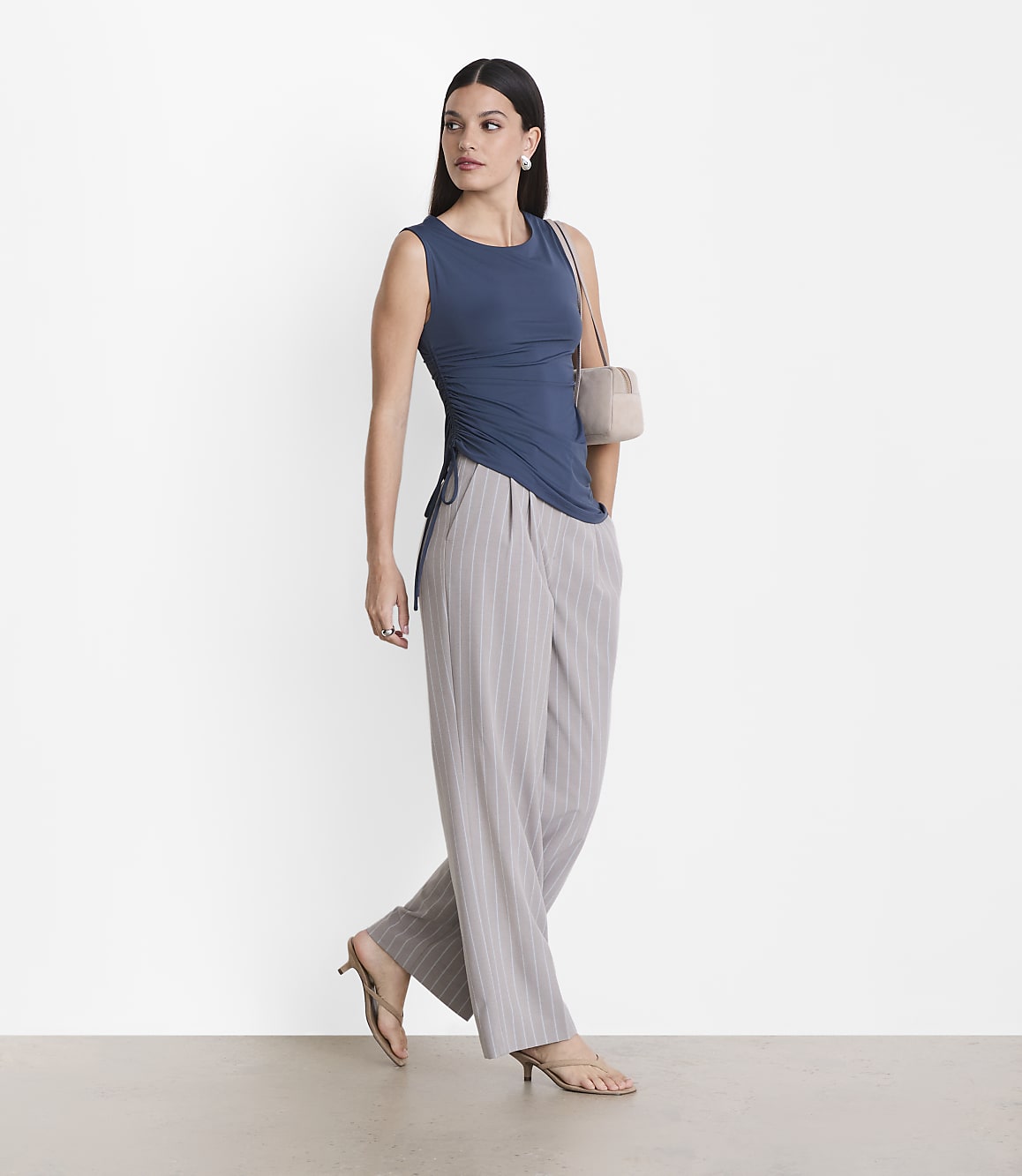 A woman in a blue top and striped pants stands against a plain white background.