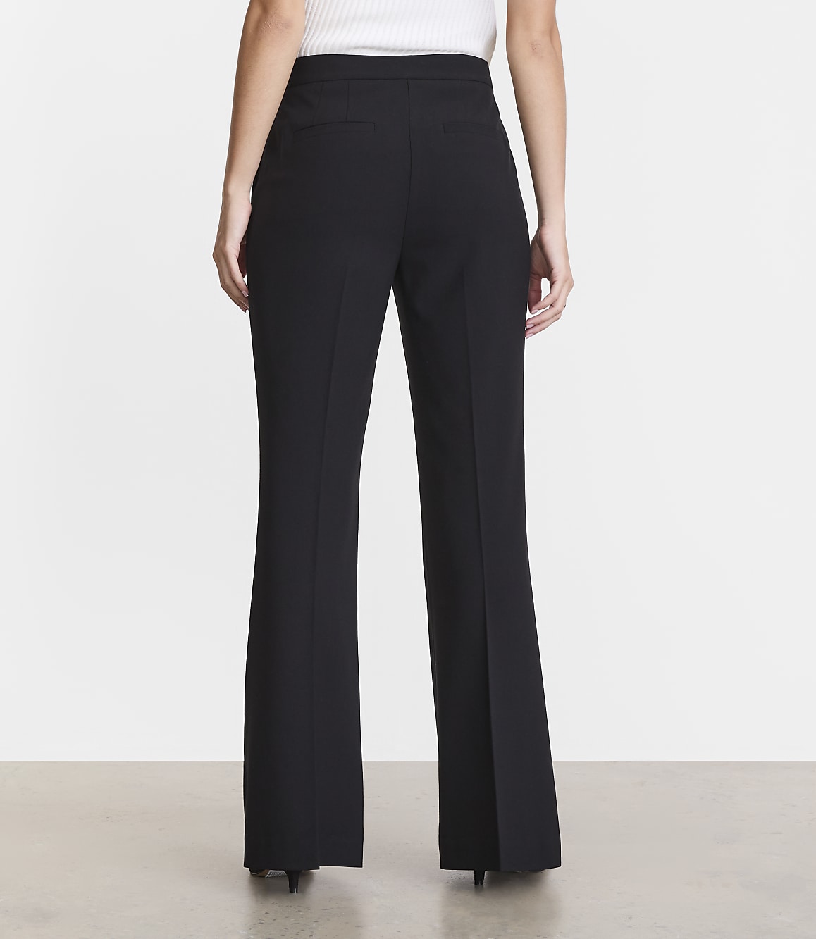 A person wearing black flared dress pants stands against a plain, light gray background.