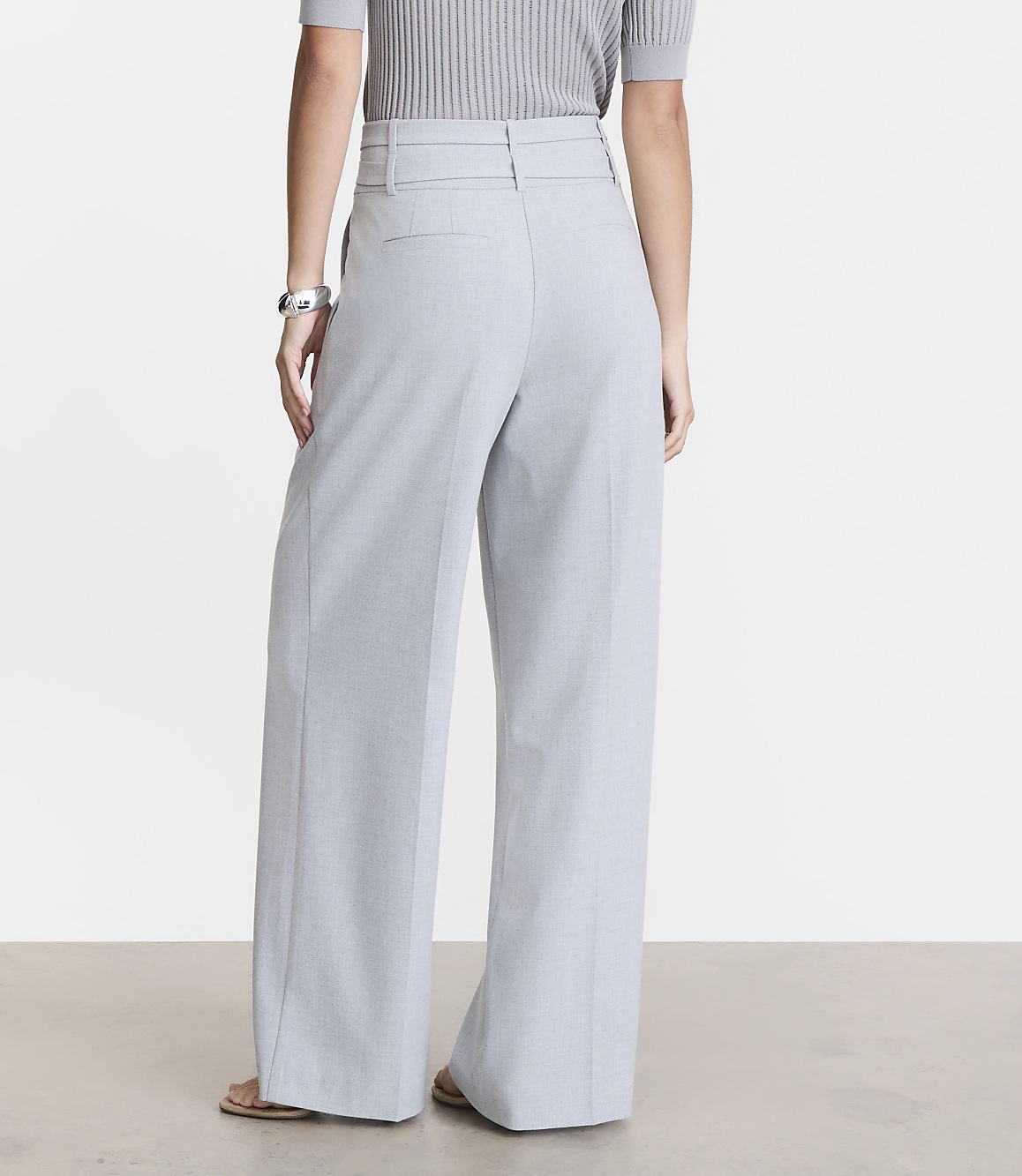 A person wearing light blue wide-leg pants and a grey ribbed top stands on a light-colored floor against a plain background.