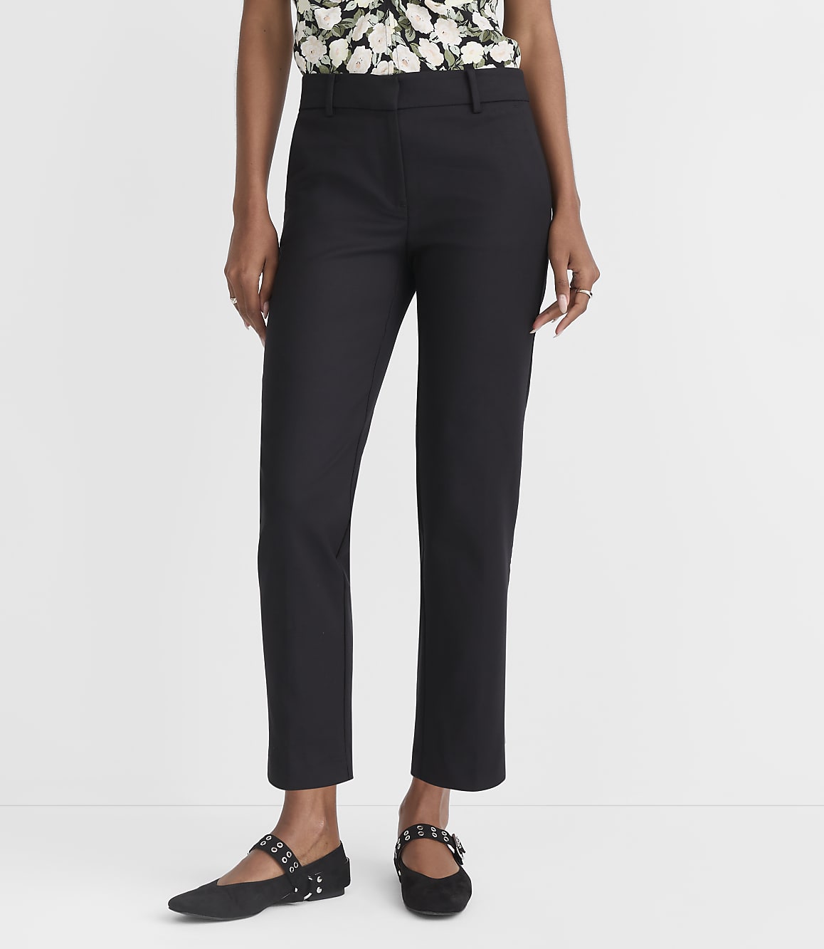 A person in black pants and a floral top stands against a plain white background.