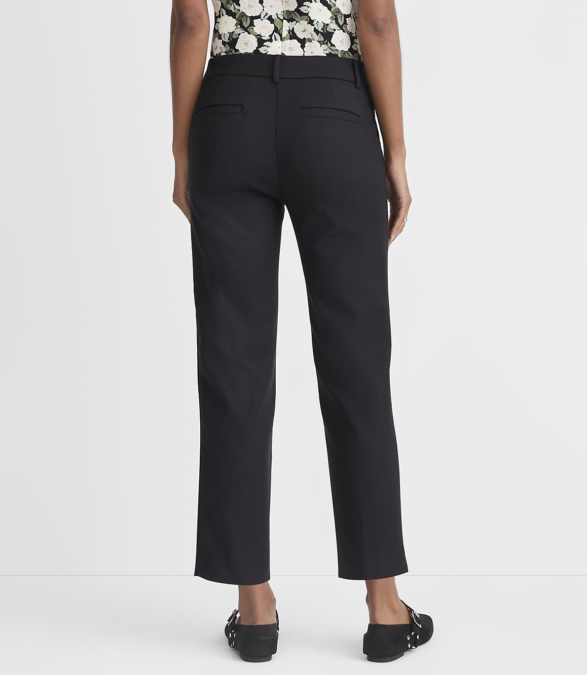 A person wearing black pants and black flats stands against a plain white background.