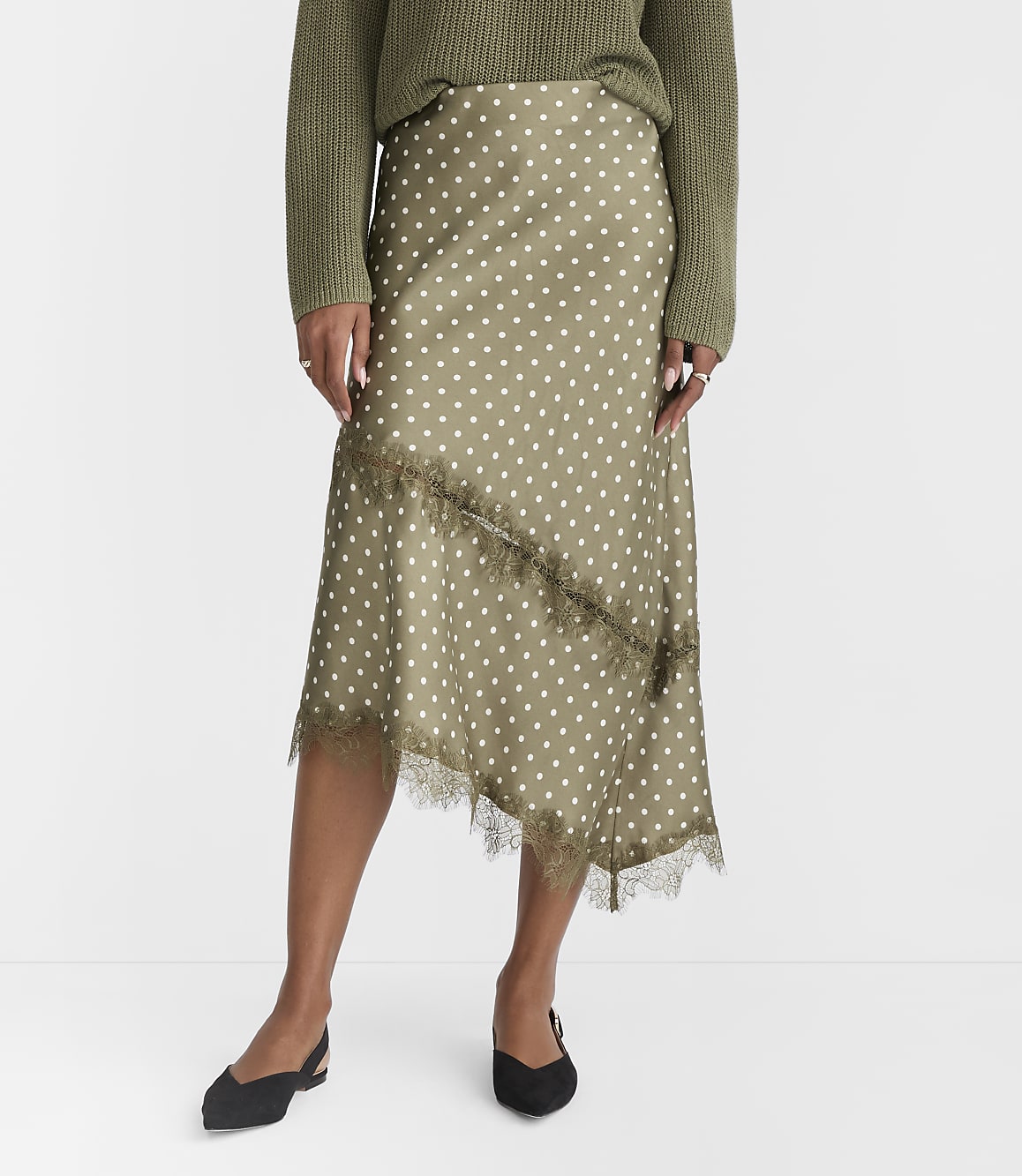 A woman in a polka dot skirt and green sweater stands against a plain white background.