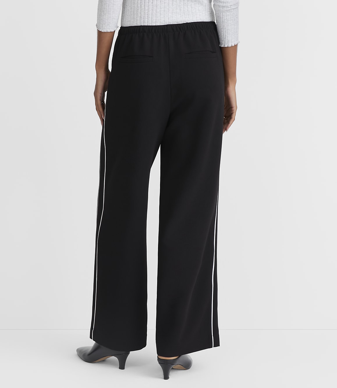 A person wearing black wide-leg pants with white piping stands against a plain white background.