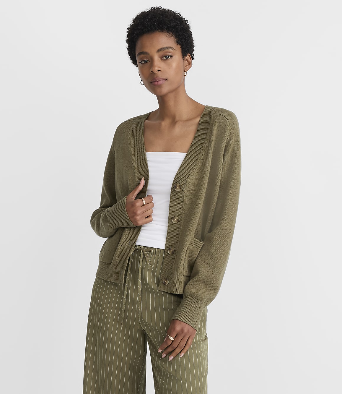 A woman in a green cardigan and striped pants stands against a plain white background.