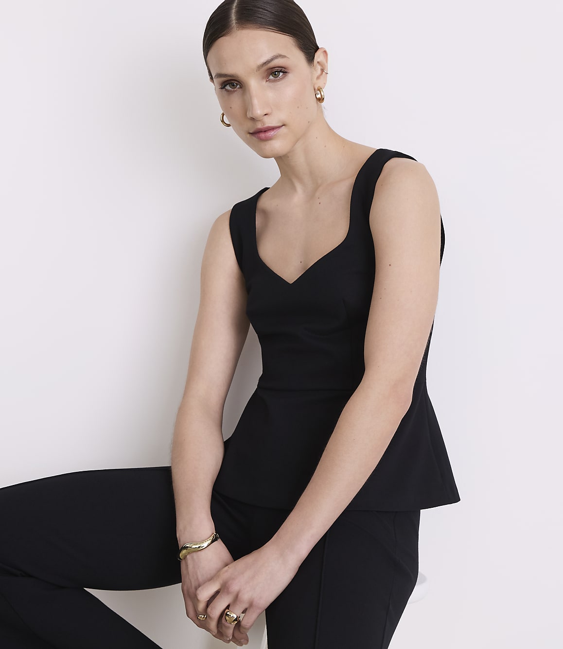 A woman in a black peplum top and pants poses against a plain white background.