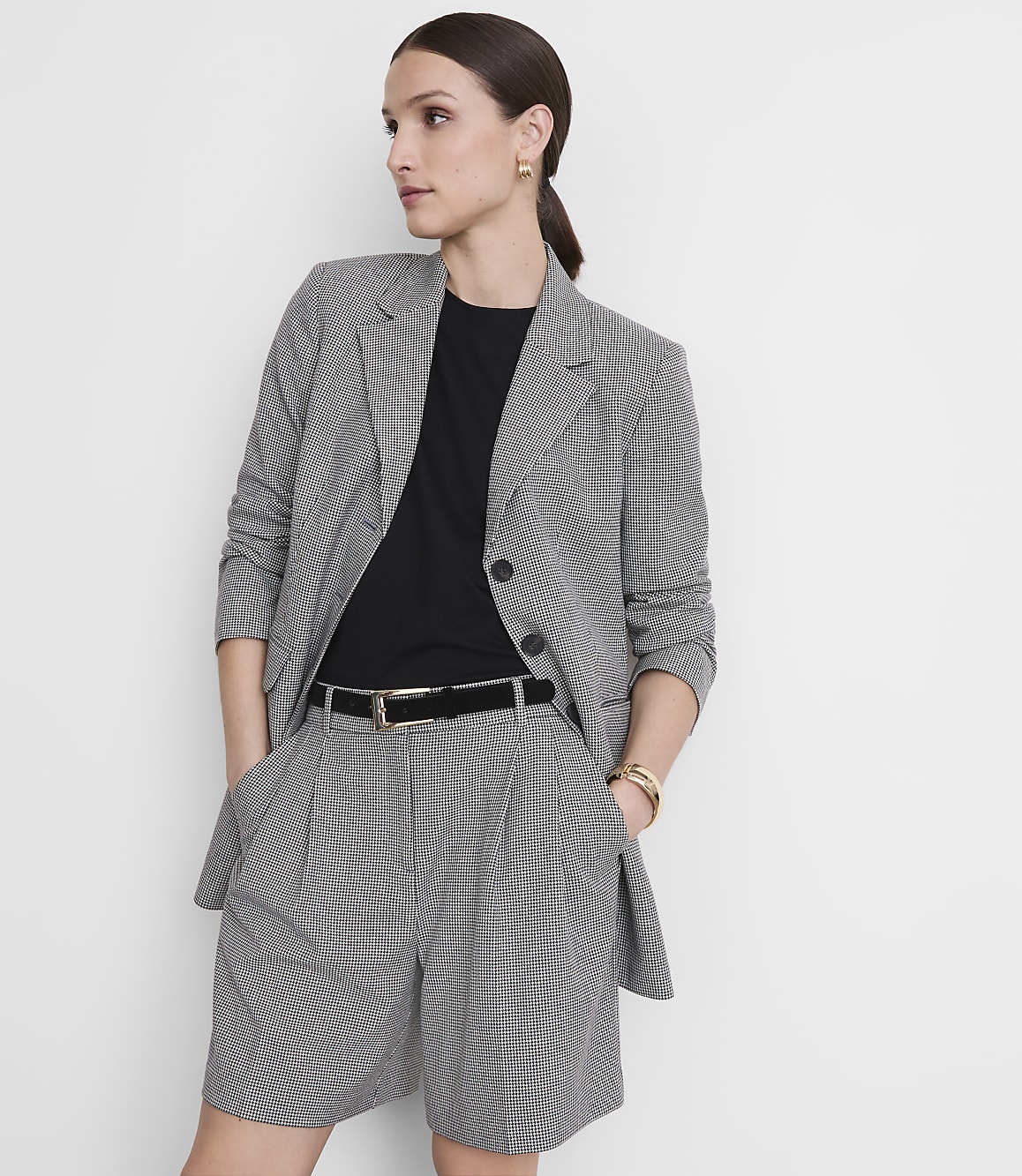 A woman in a black and white checkered blazer and shorts stands against a plain white background.