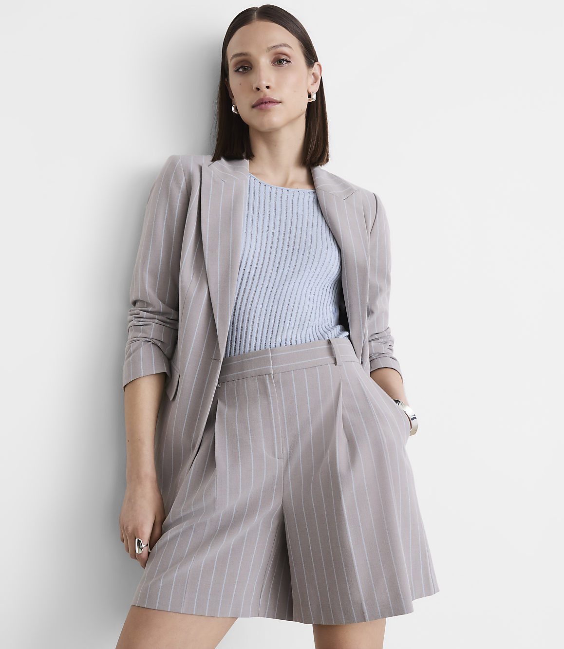 A woman in a pinstripe suit stands against a plain white wall.