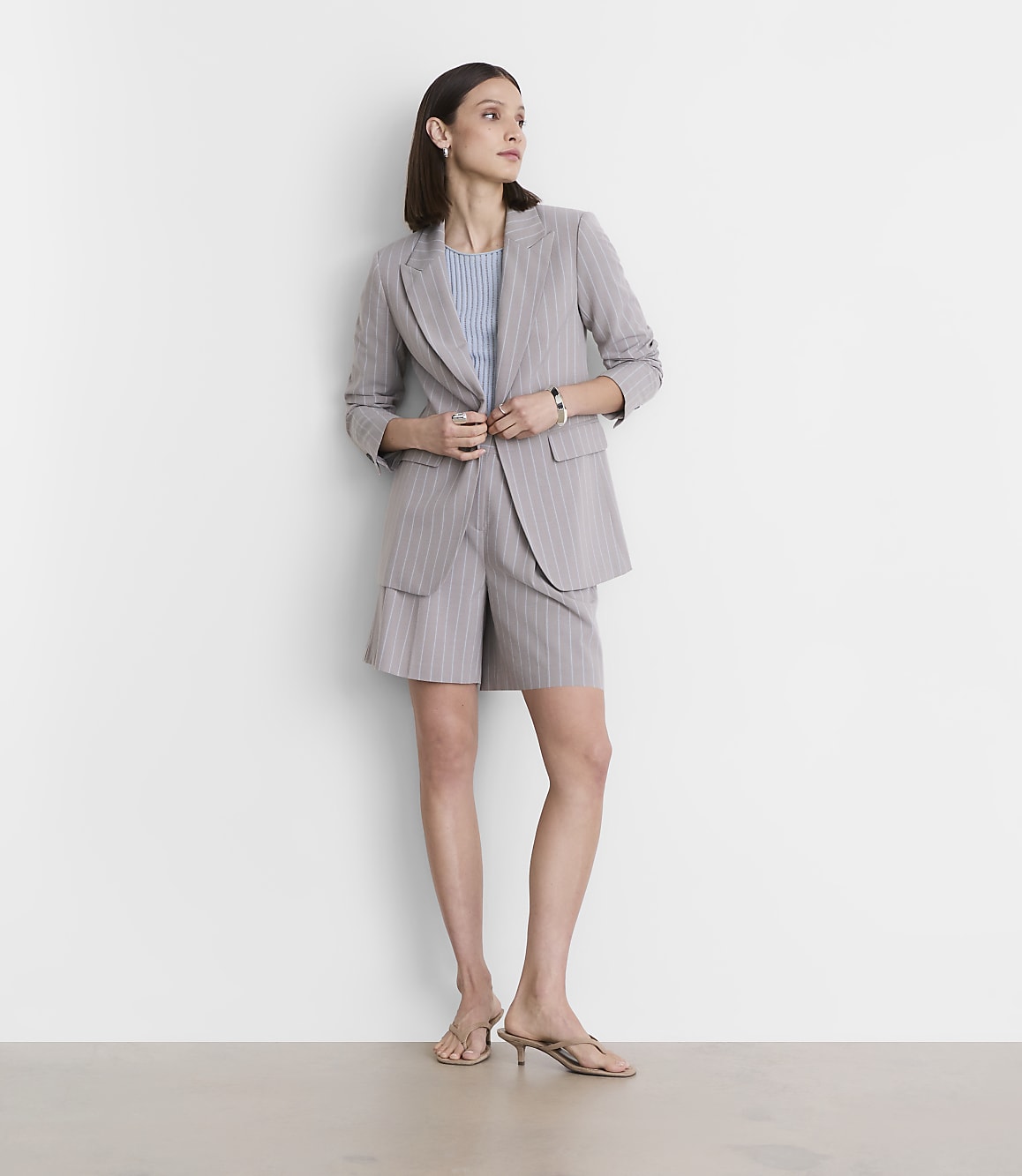 A woman in a pinstripe suit stands against a plain white wall.