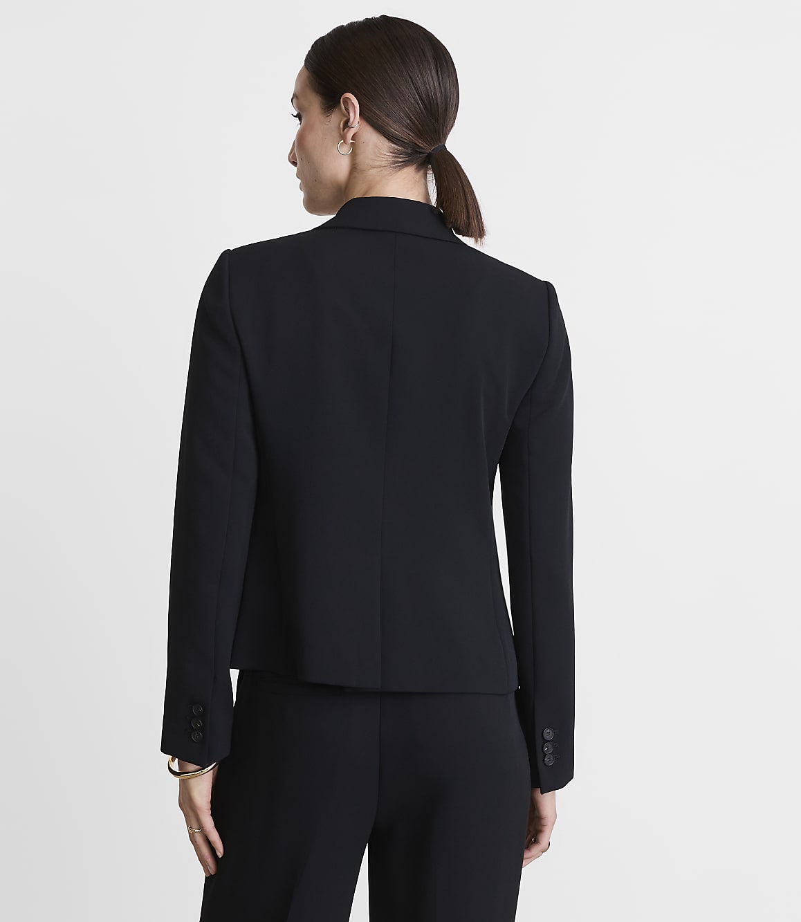 A woman in a black blazer and pants stands against a plain white background.