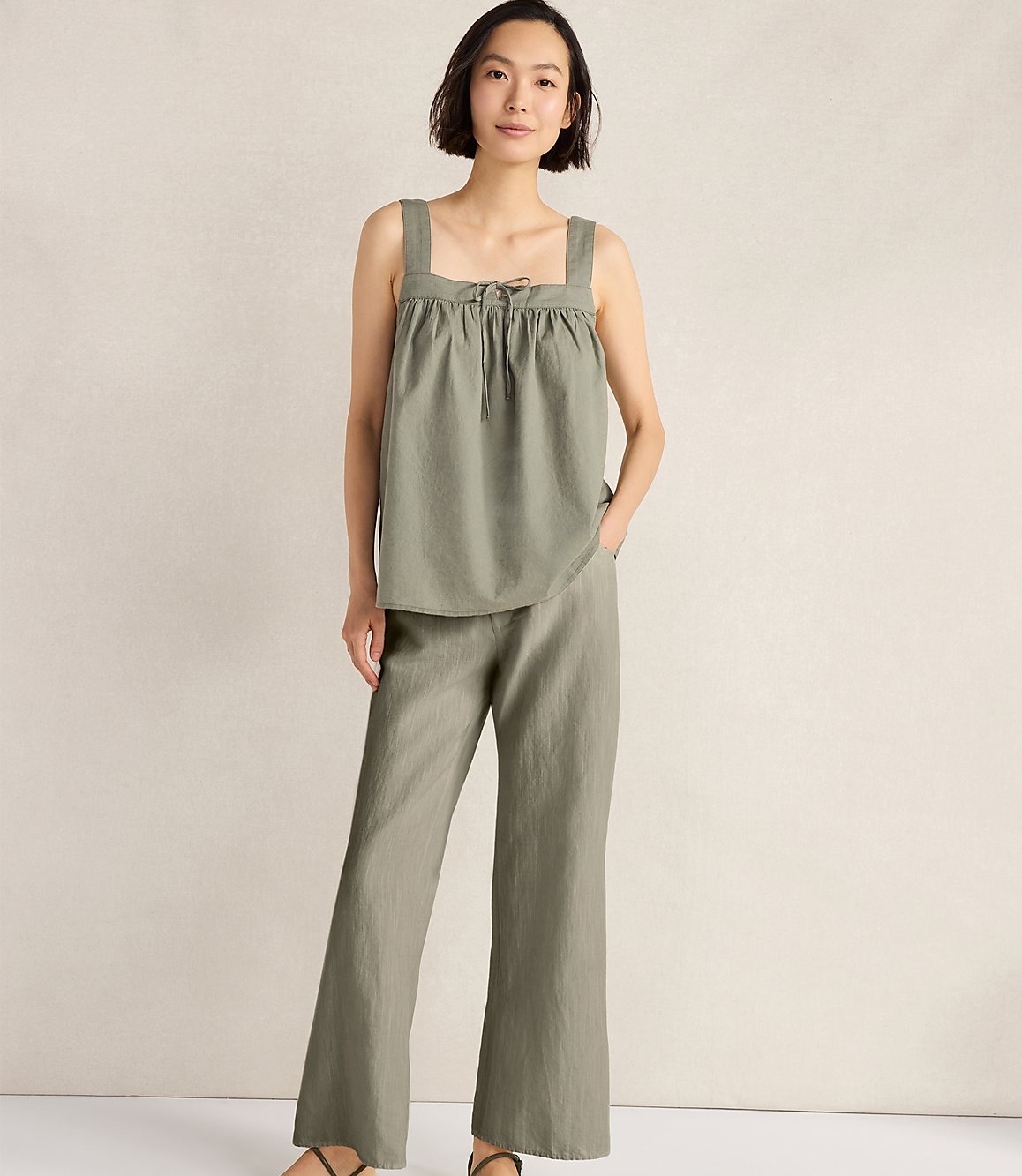 A woman in a green linen set stands against a textured beige background.