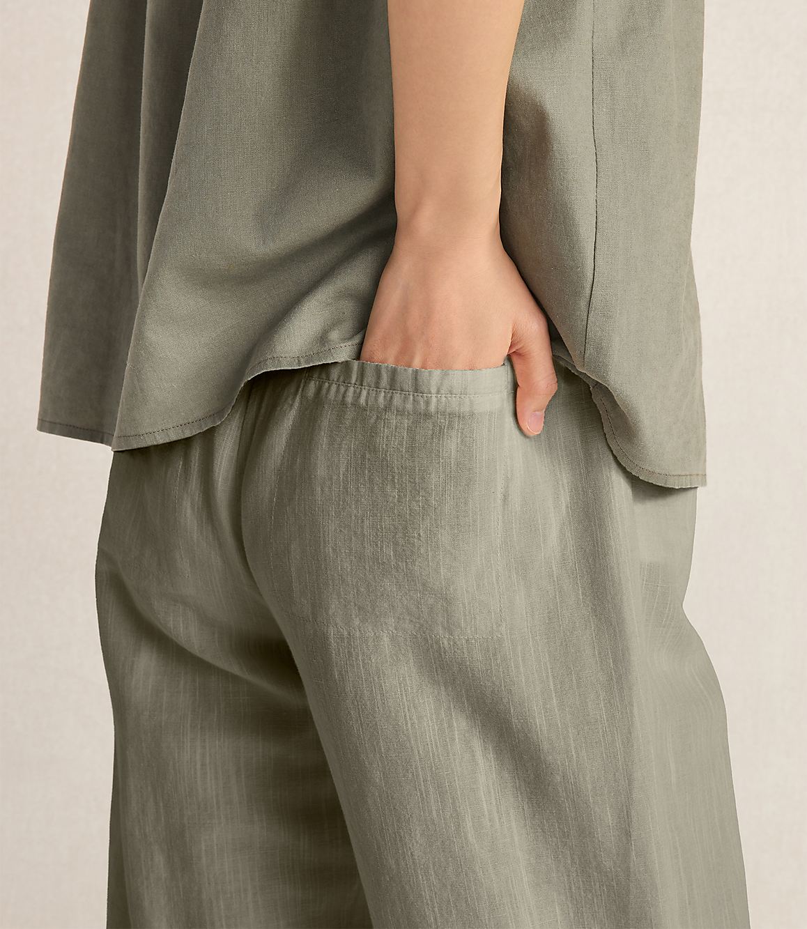 A hand rests in the pocket of loose-fitting, olive-green pants against a plain, light-colored background.