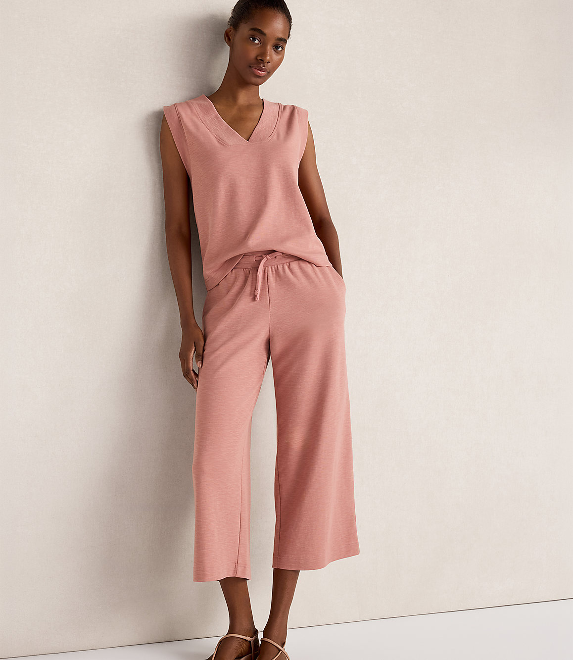 A woman in a pink loungewear set stands against a plain, light-colored wall.
