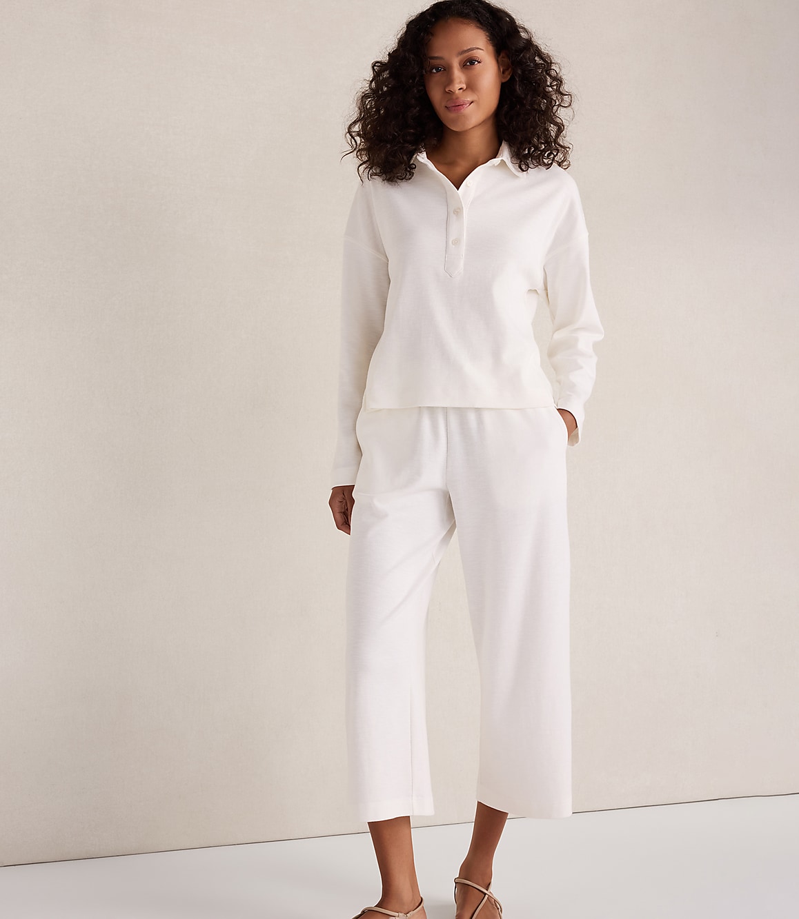 A woman in a white loungewear set stands against a textured, light-colored wall.