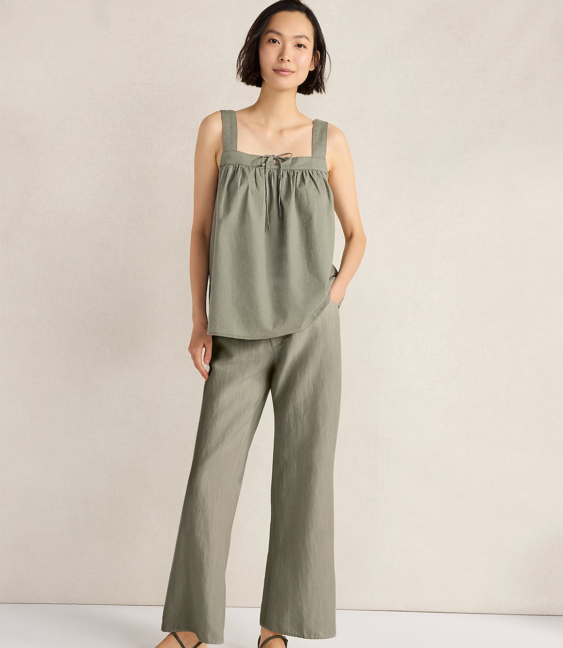A woman in a green linen set stands against a textured, light-colored wall.