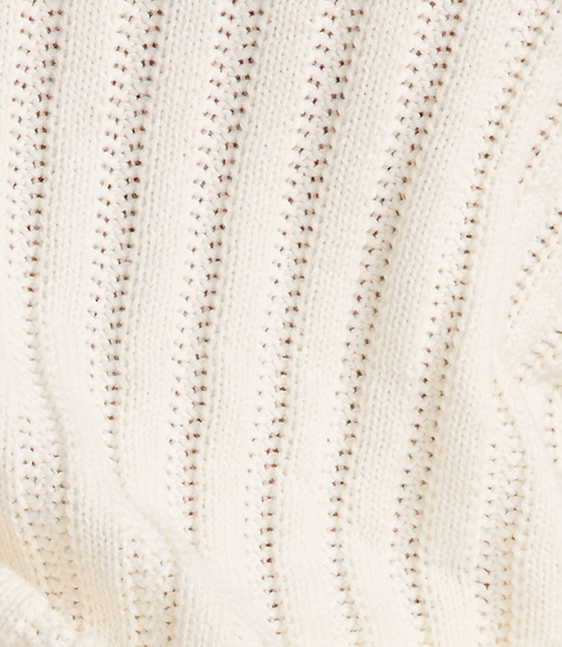 A close-up of a cream-colored knitted fabric with vertical ribbed texture and small holes fills the frame.