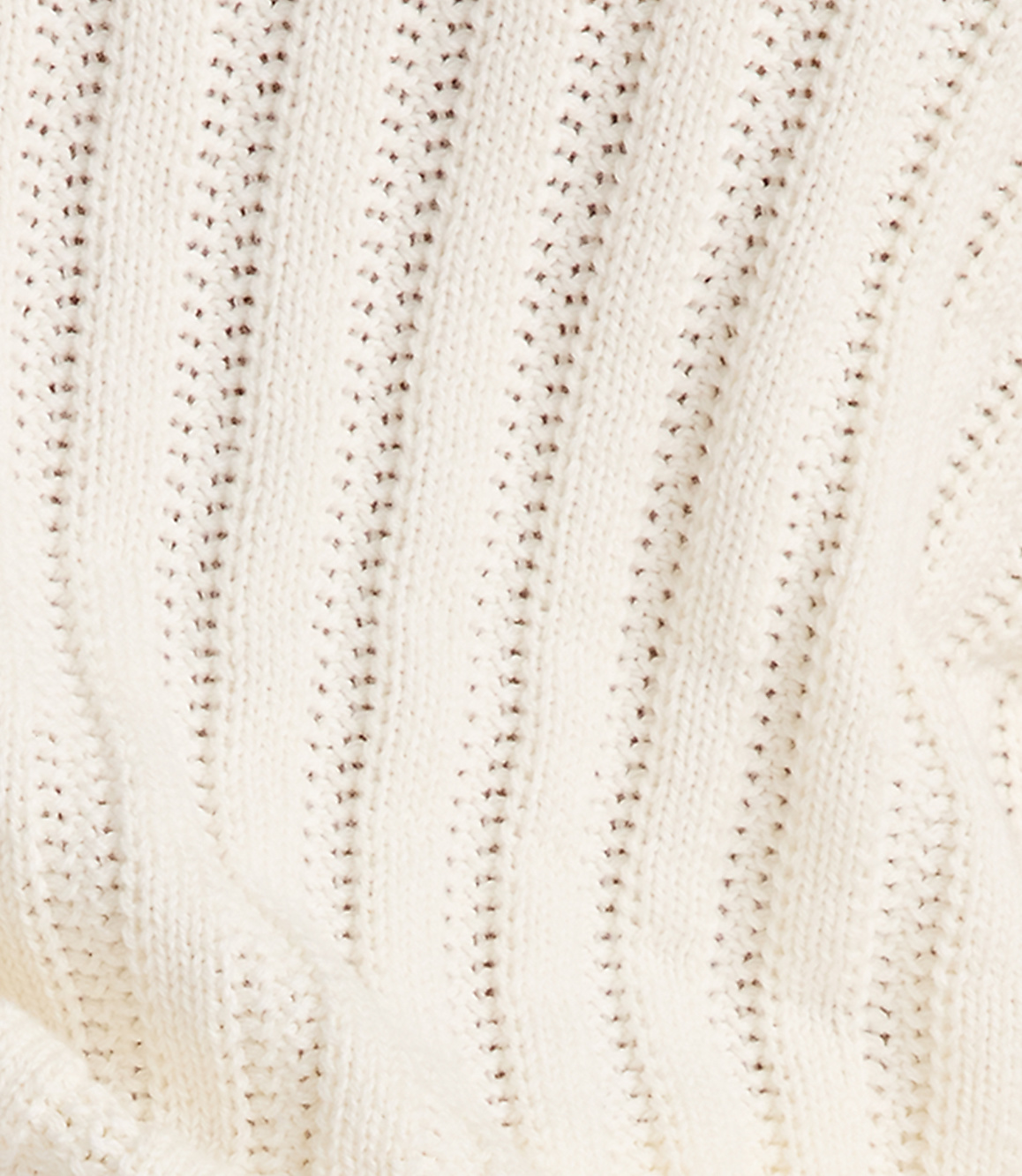 A close-up view of a cream-colored knitted fabric with a ribbed texture and small holes in the foreground, against a softly blurred background of the same material.
