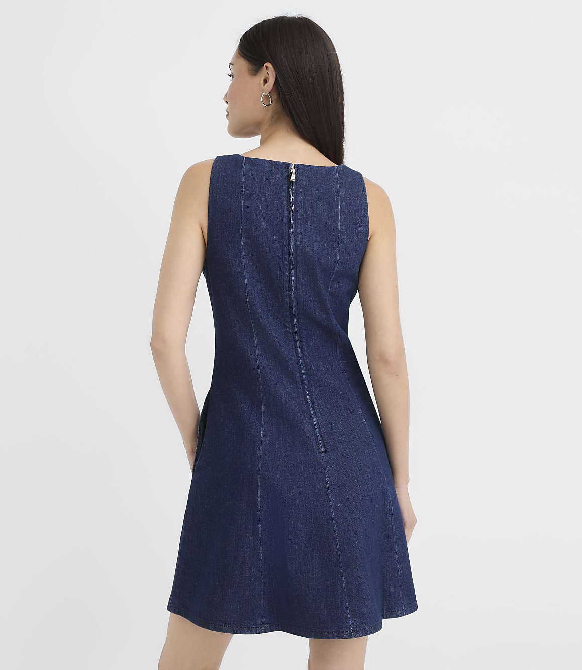 A woman in a denim dress stands against a plain white background.