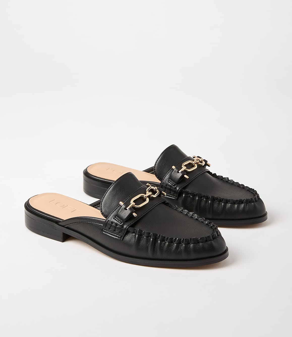 A pair of black leather mules with gold chain accents rests on a plain white background.