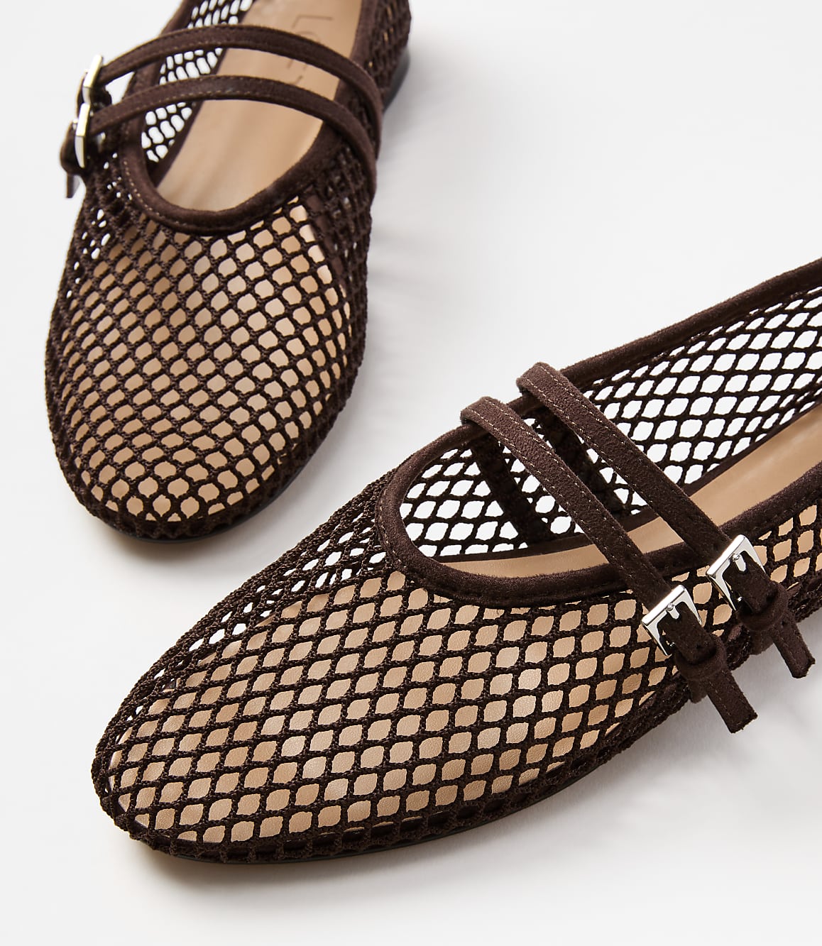 A pair of brown mesh ballet flats with double ankle straps are in the foreground against a plain white background.