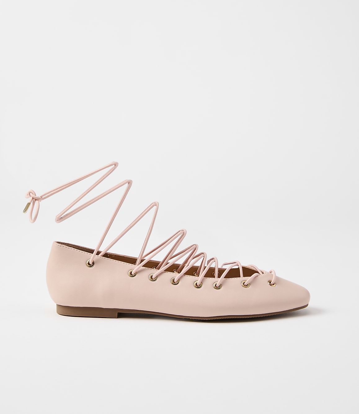 A pale pink ballet flat with long, crisscrossing laces is presented against a plain white background.