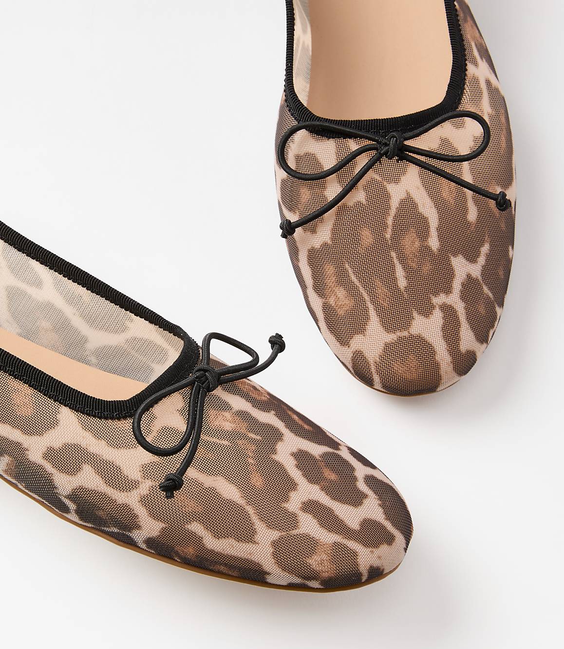 A pair of sheer leopard-print ballet flats with black bows rests on a white background.