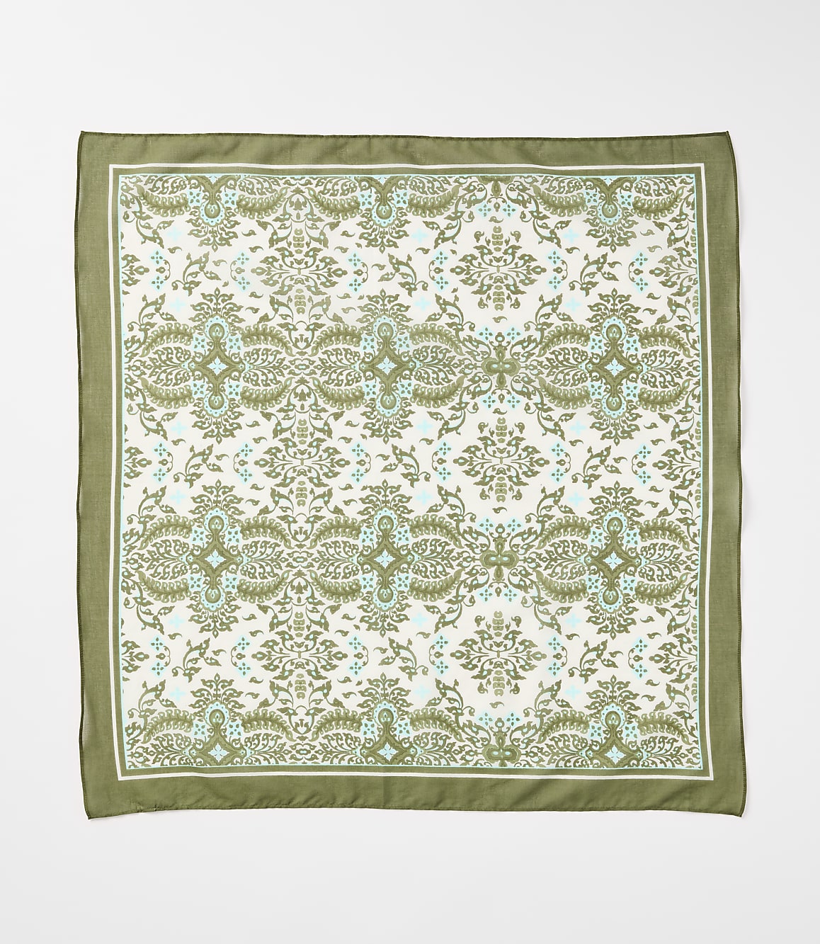 A square silk scarf with a repeating damask pattern in green and light blue on a cream background is laid flat against a white surface.