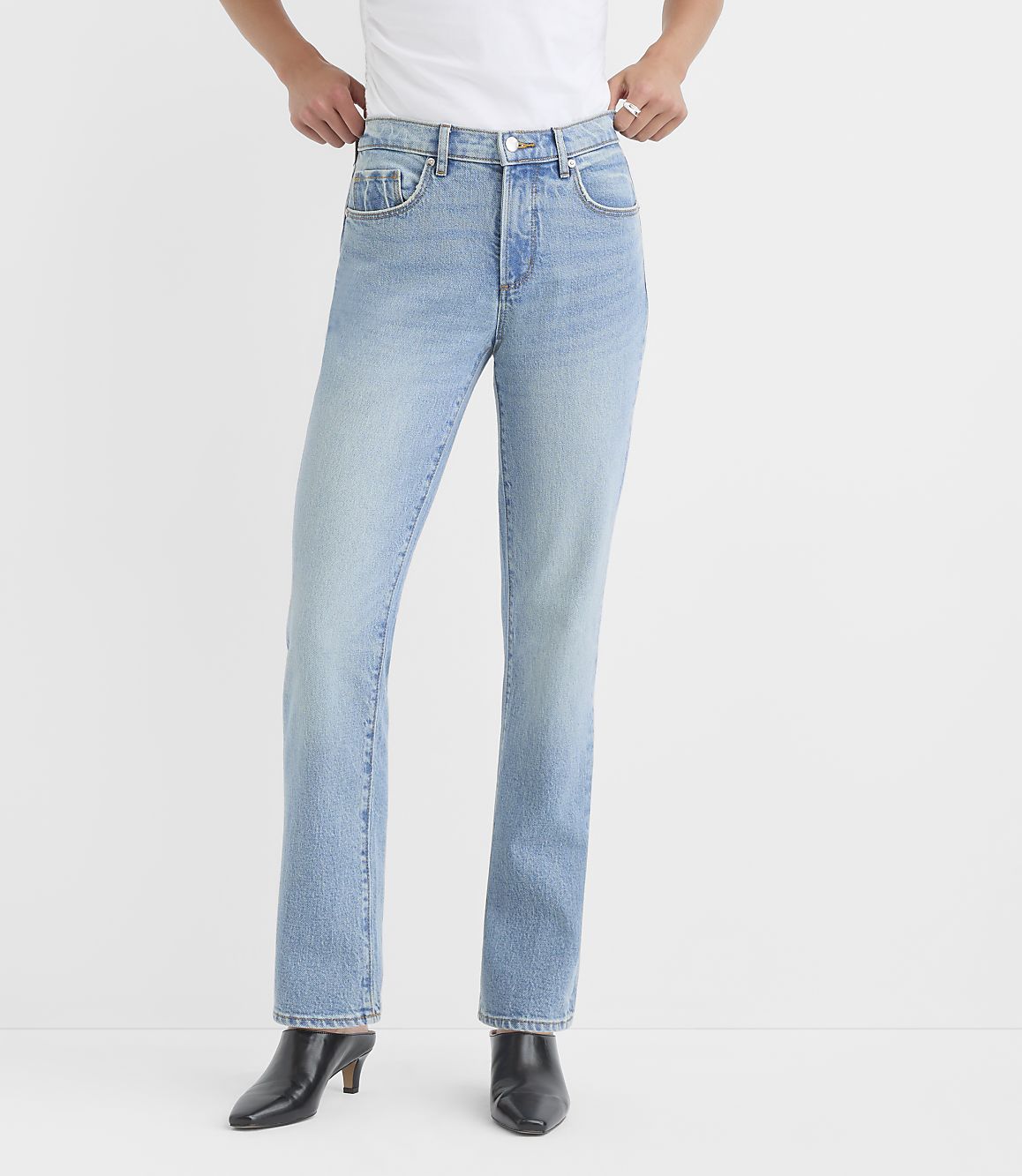 A person stands in light-wash denim jeans and black heeled boots against a plain white background.