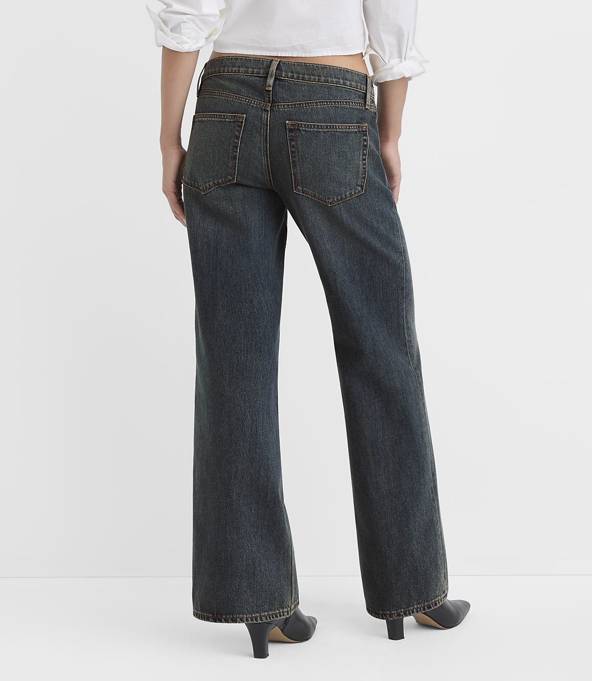 A person wearing dark wash flared jeans and a white top stands against a plain white background.