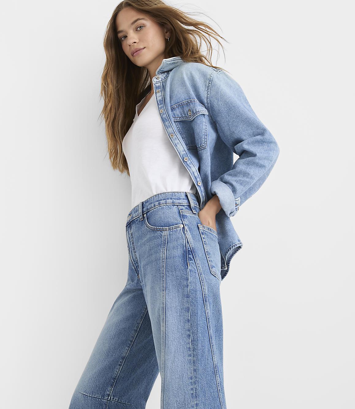 A woman in a denim shirt and jeans stands against a plain white background.