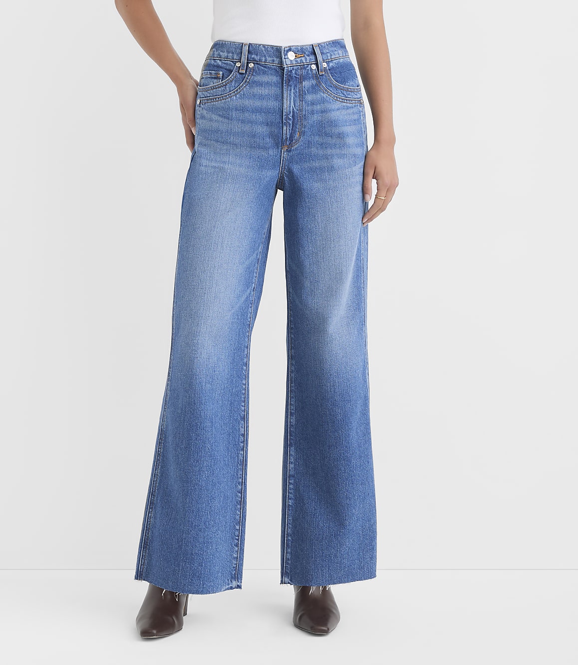 A person stands in wide-leg blue jeans and brown shoes against a plain white background.
