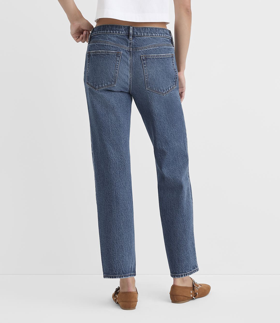 A person wearing blue jeans and brown loafers stands against a plain white background.