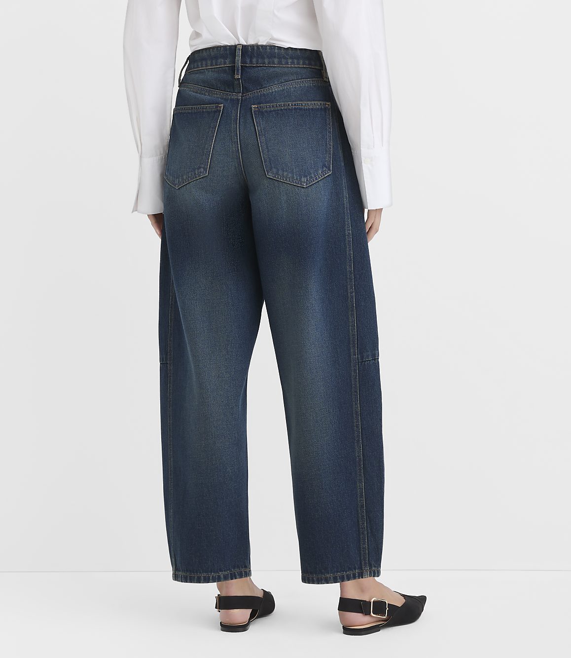 A person in a white shirt and baggy blue jeans stands against a plain white background.