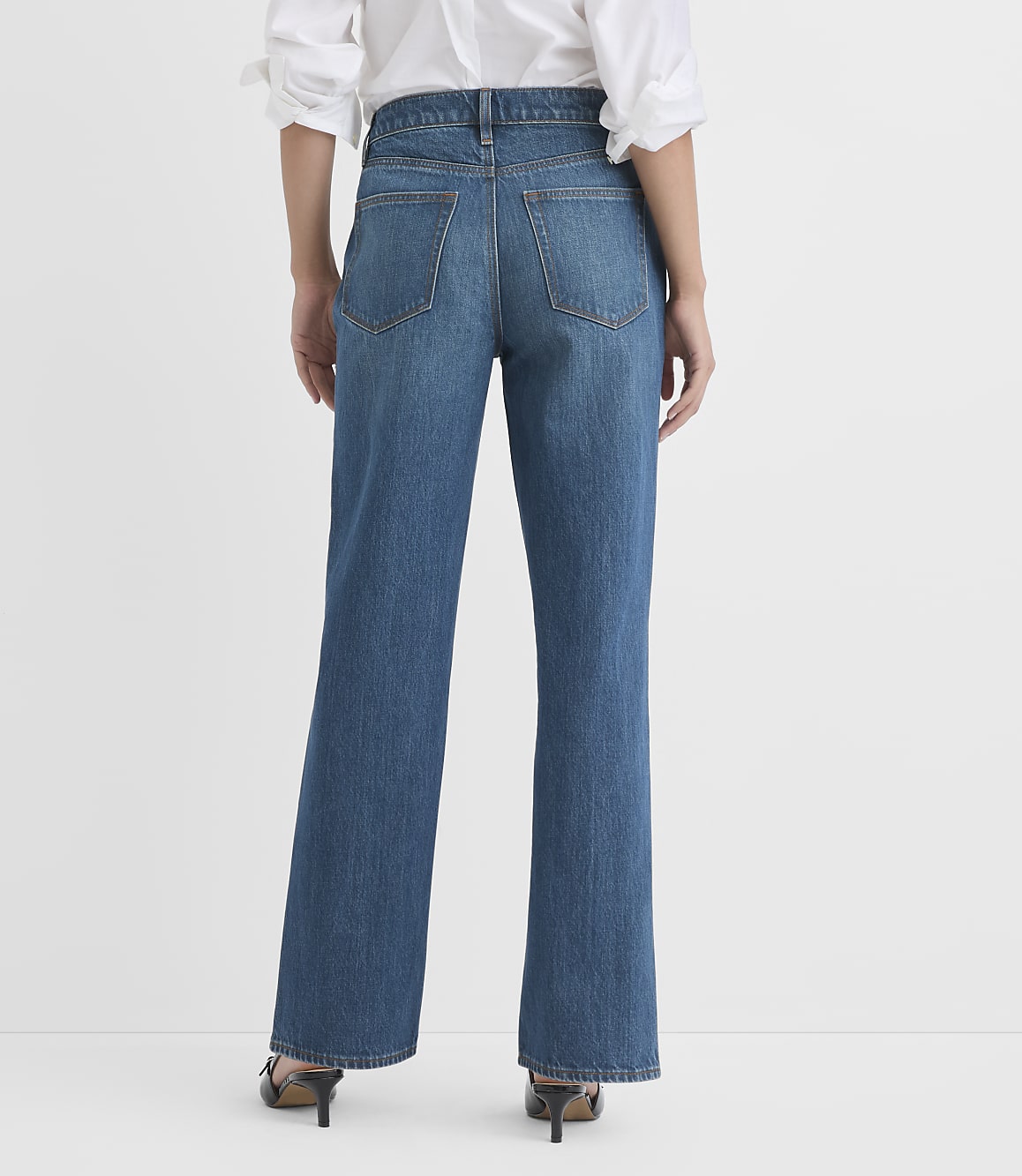 A person wearing blue jeans and a white shirt stands against a plain white background.