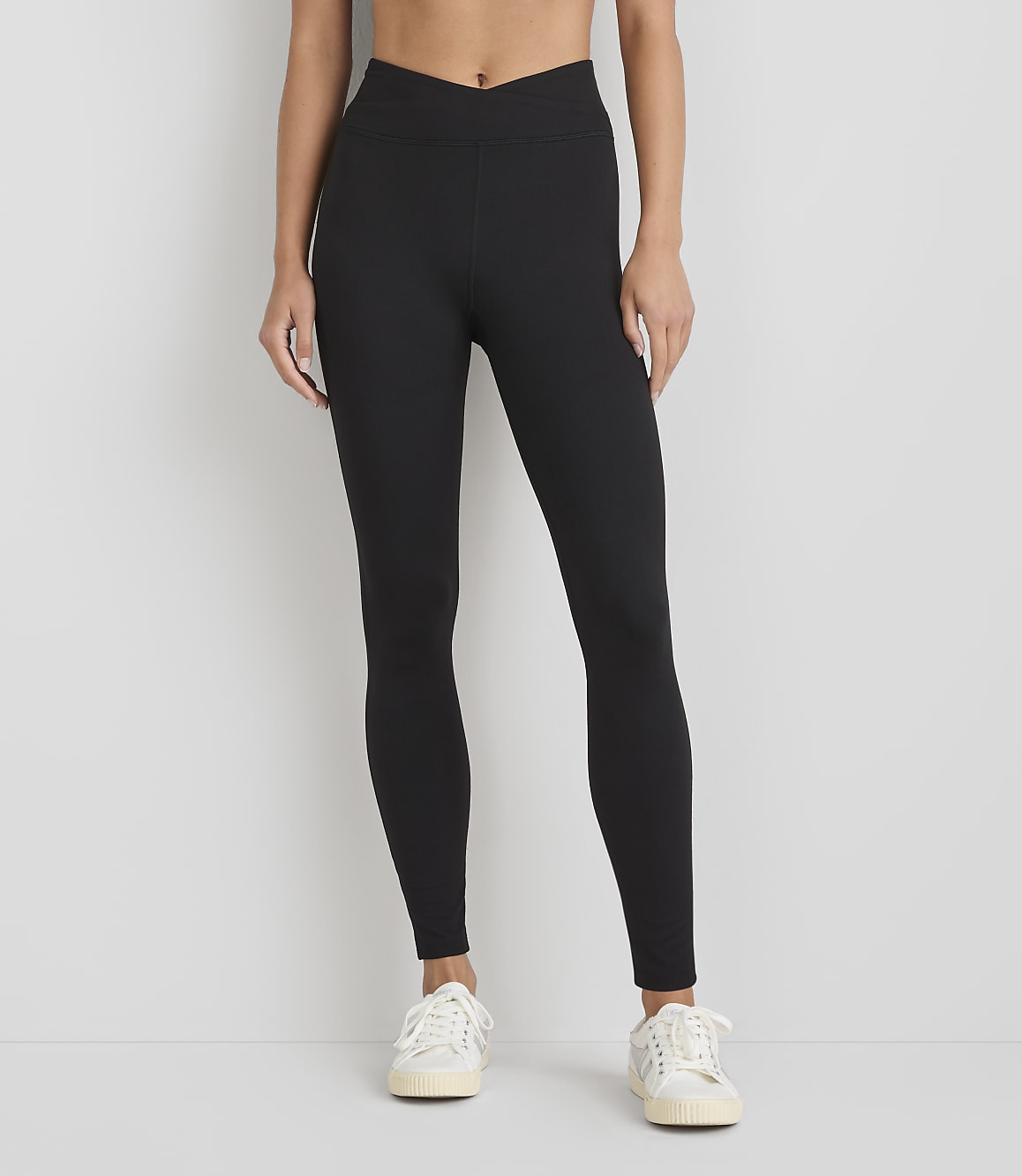 A woman wearing black leggings and white sneakers stands against a plain white background.