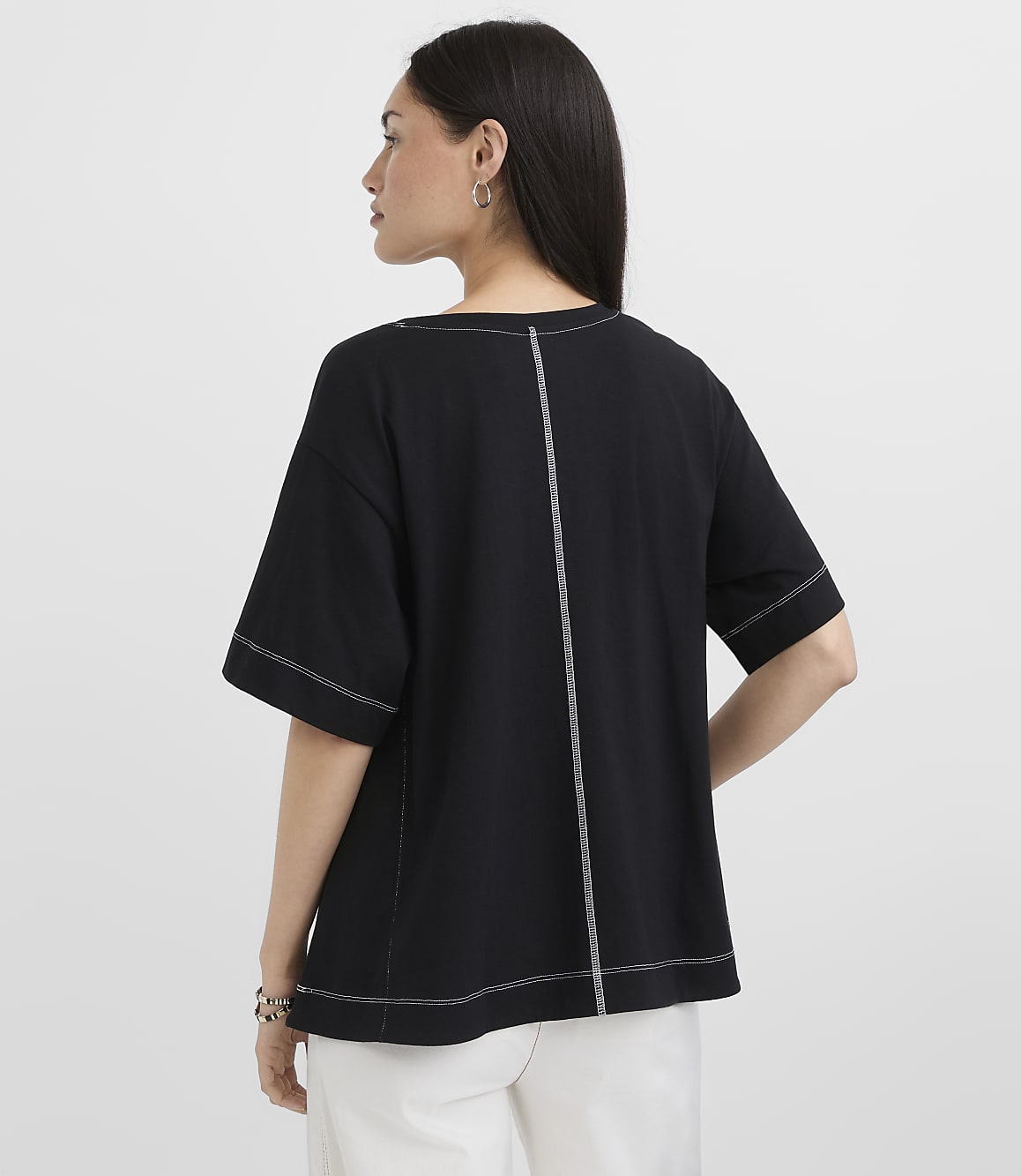 A woman in a black t-shirt with white stitching stands against a plain white background.