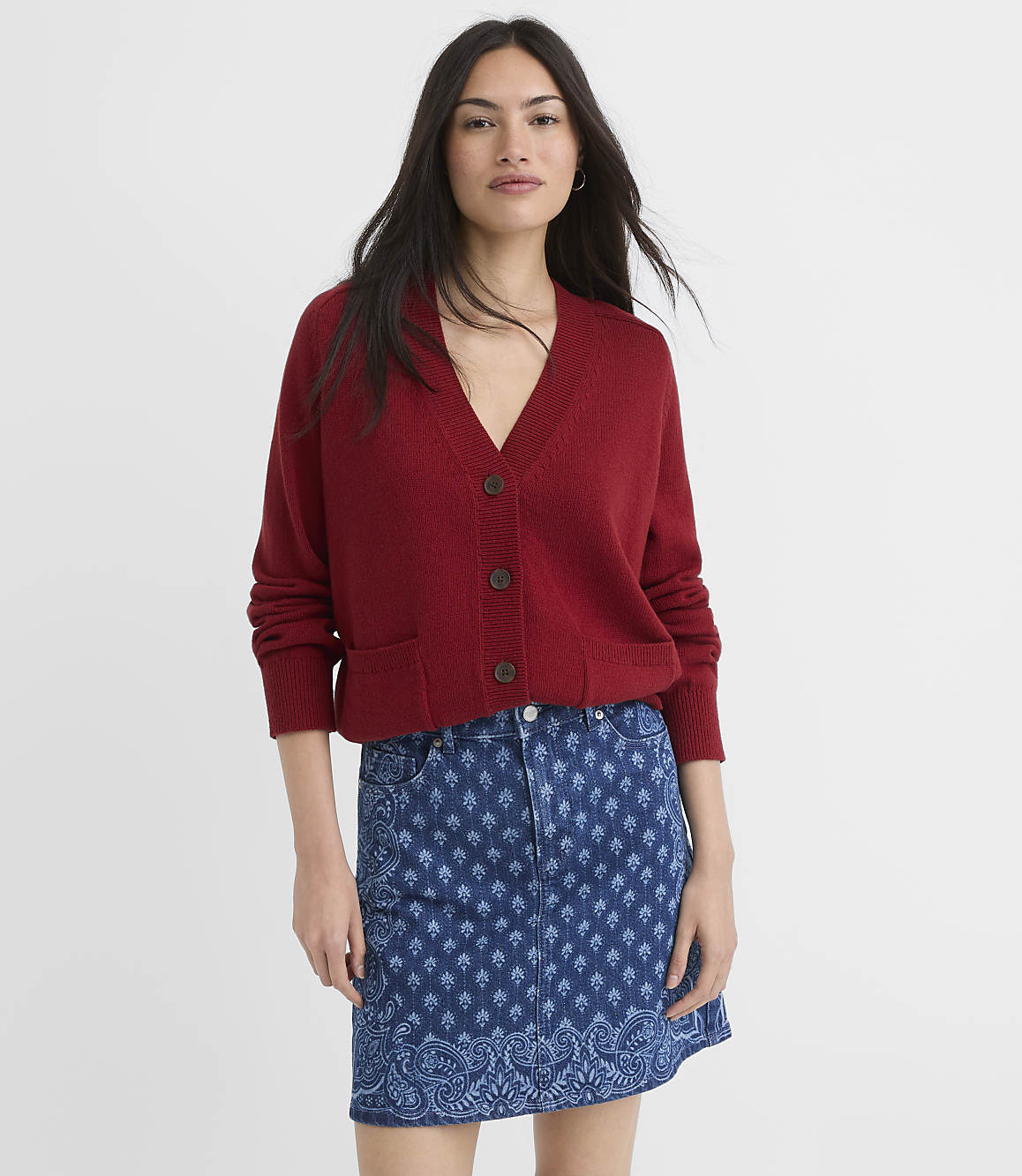 A woman in a red cardigan and patterned denim skirt stands against a plain white background.
