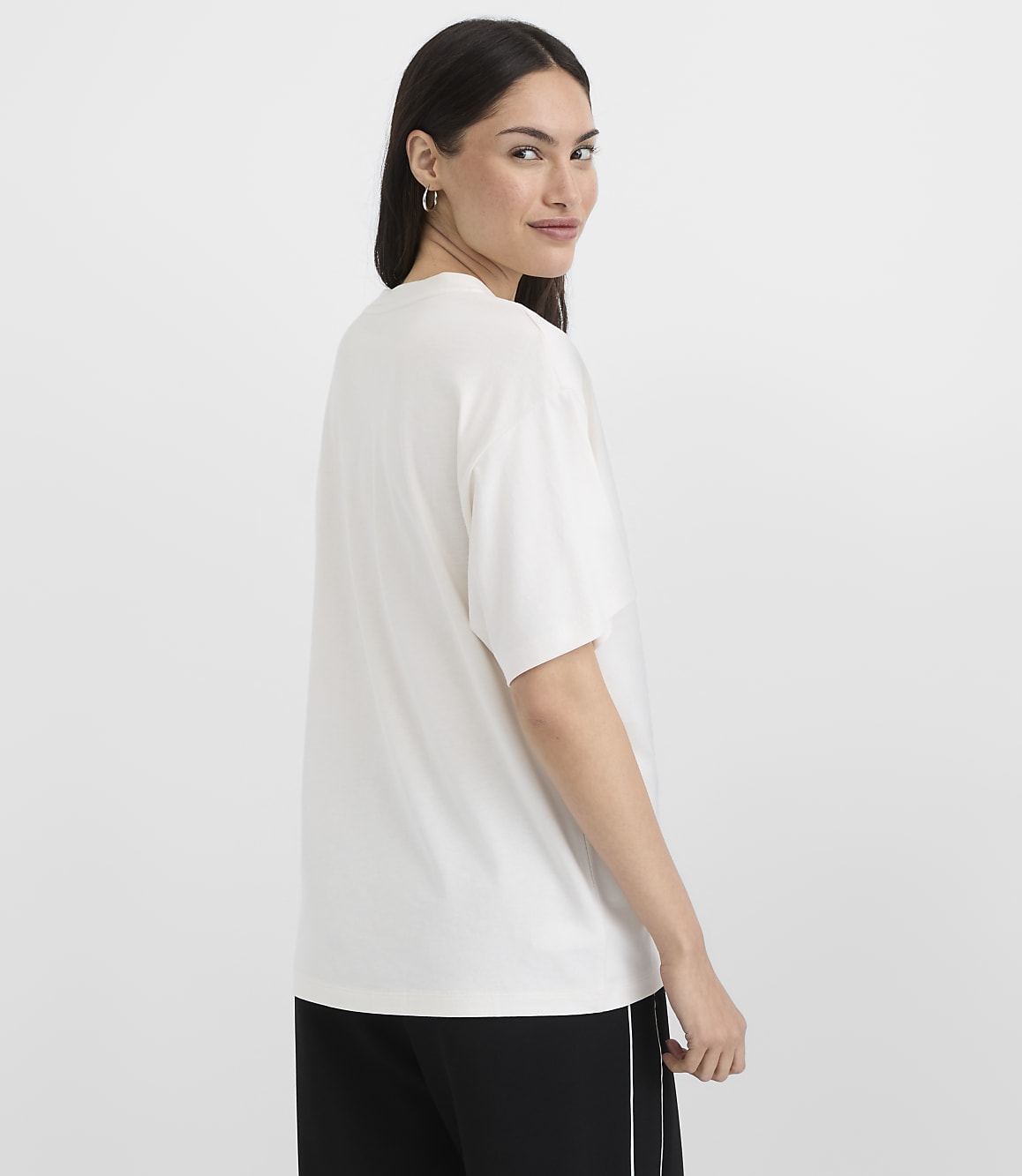 A woman in a white t-shirt and black pants stands against a plain white background.