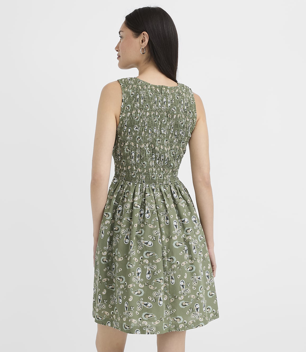 A woman in a green paisley print dress stands against a plain white background.