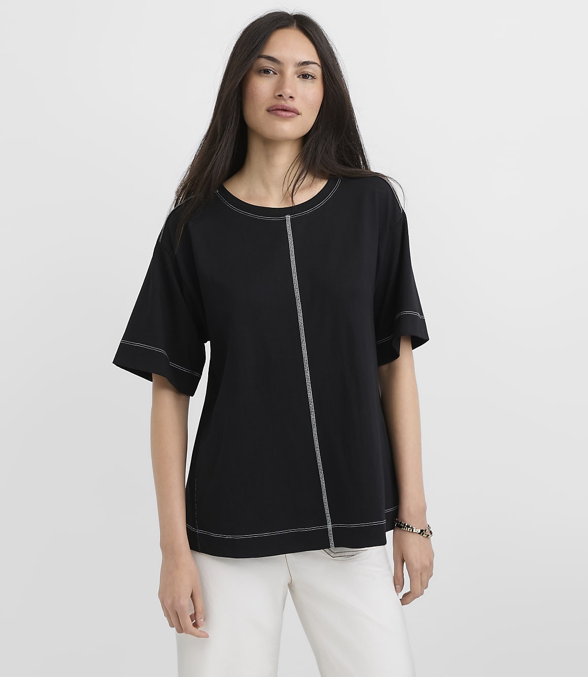 A woman in a black t-shirt with white stitching stands against a plain white background.